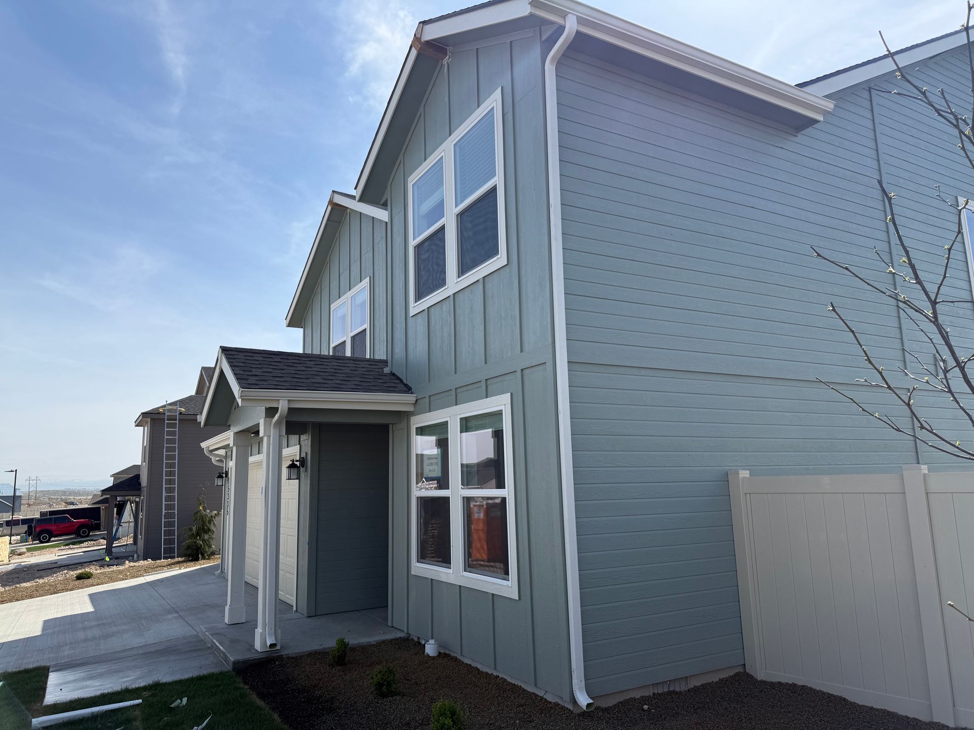 Two-story blue house with white trim. Clear sky, concrete walkway, and beige fence.
