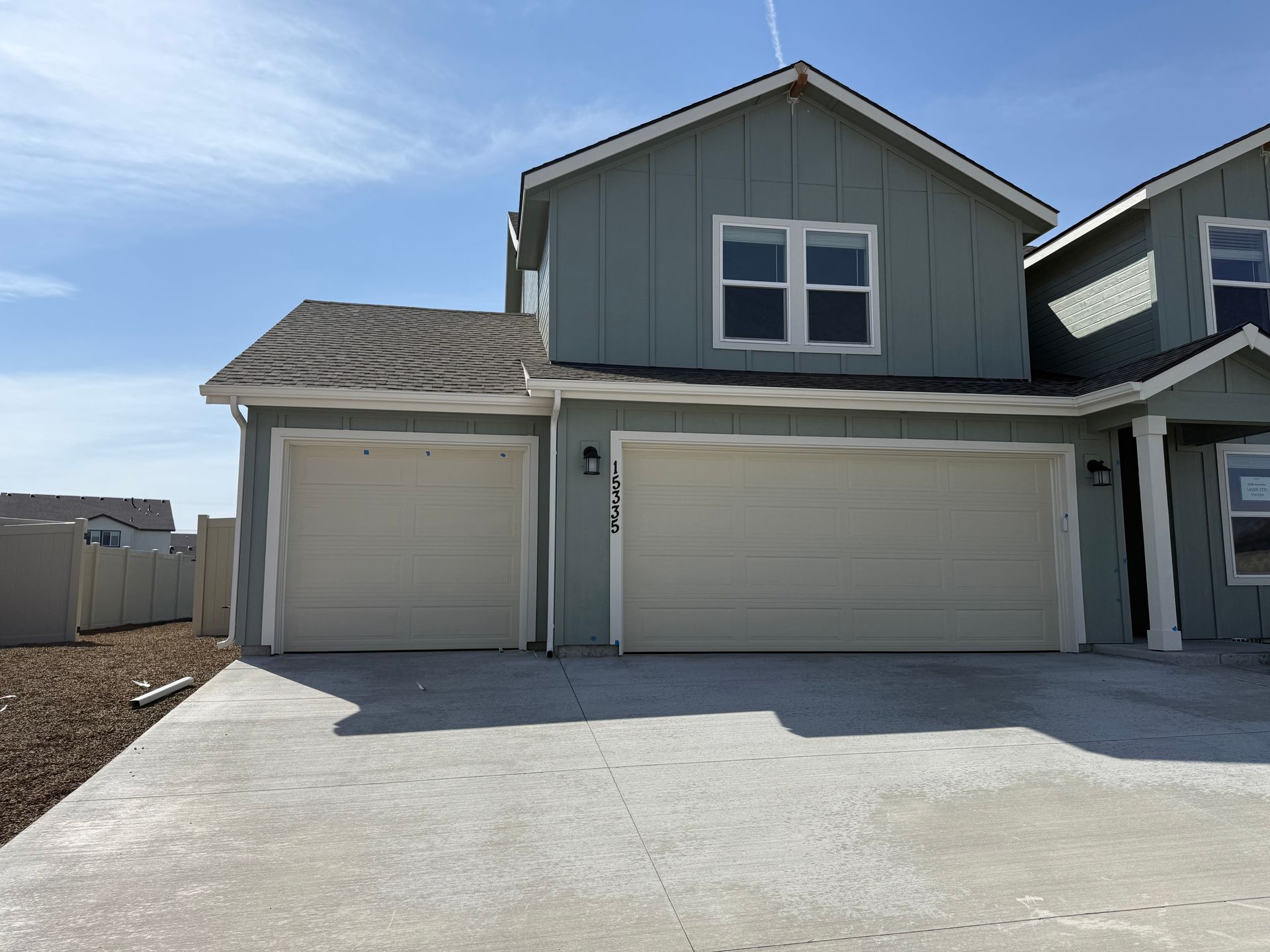 Two-story house with two-car garage, light blue siding, and concrete driveway on a sunny day.