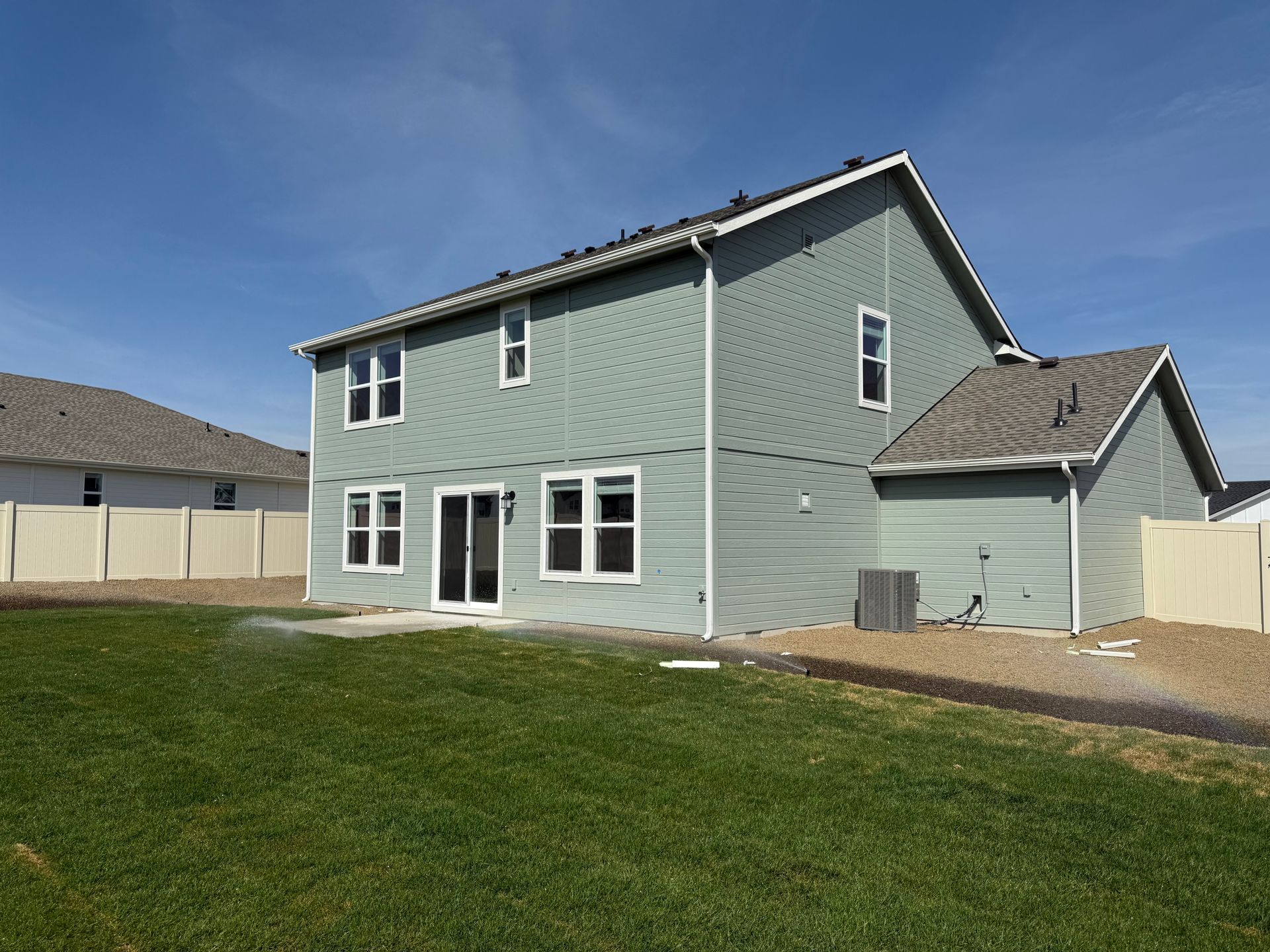 Two-story house with green siding, white trim, and a fenced backyard on a sunny day.