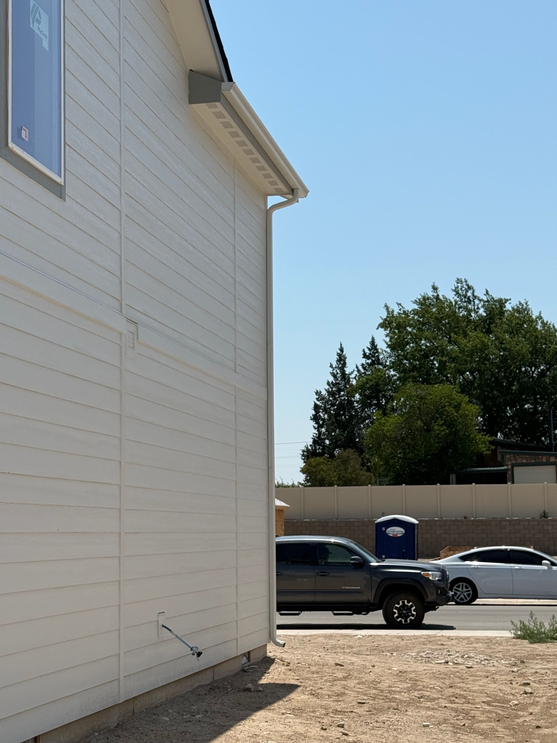 White house exterior with a gutter. A truck and car parked on street with a blue portable toilet.