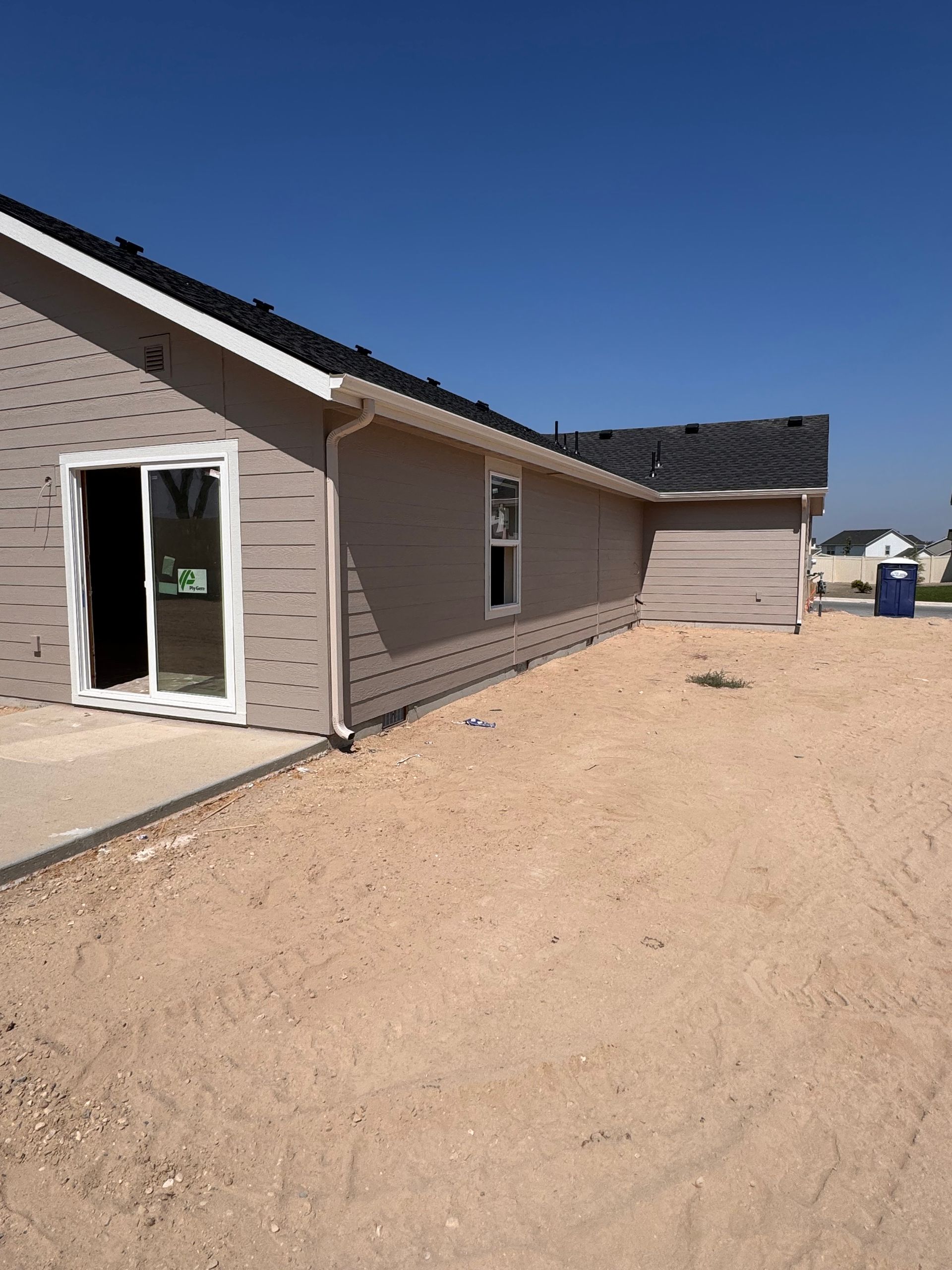 Exterior view of a new house under construction, with beige siding, white trim, and a clear blue sky.