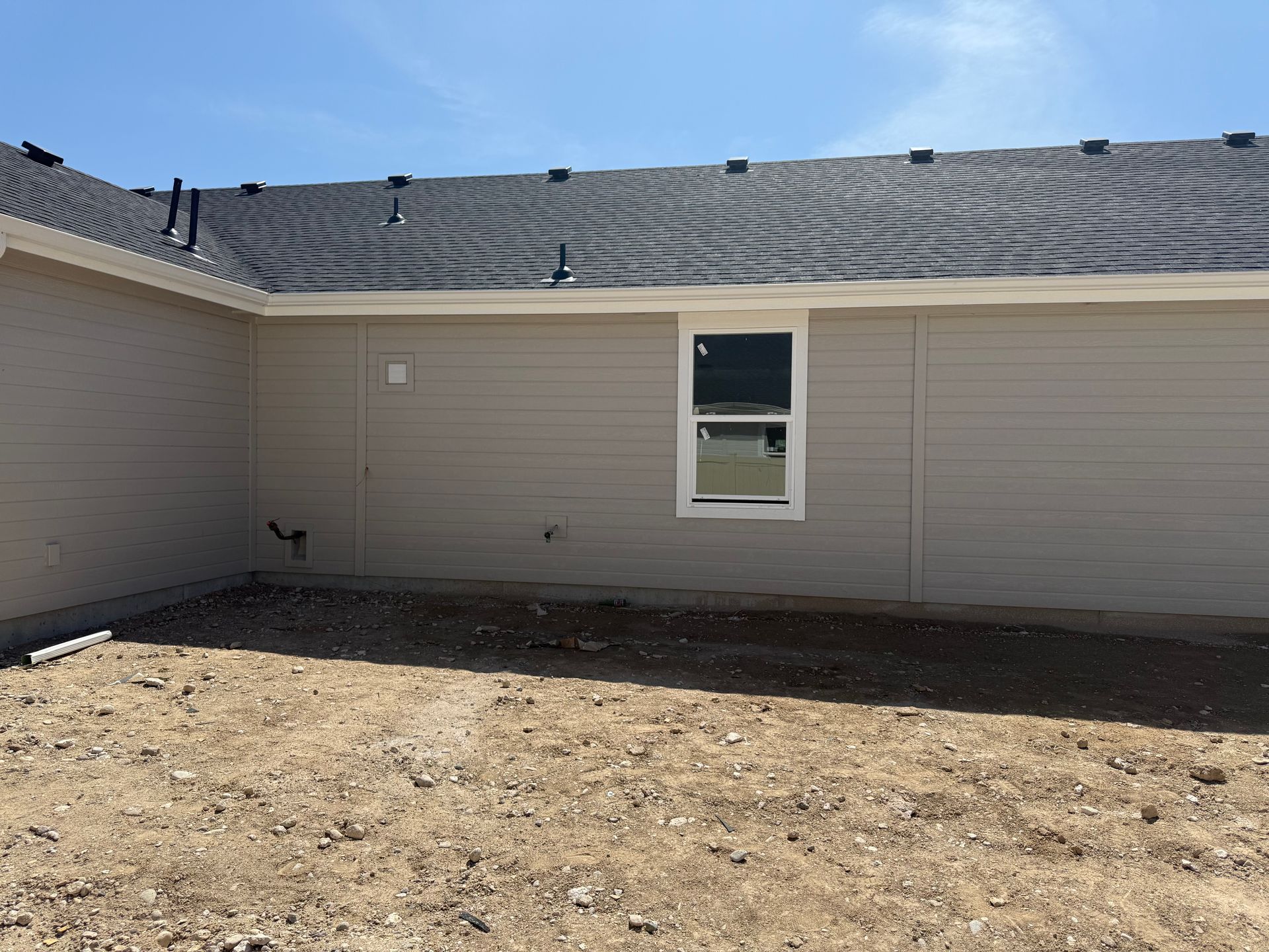 Tan house exterior with a window and black roof against a blue sky.