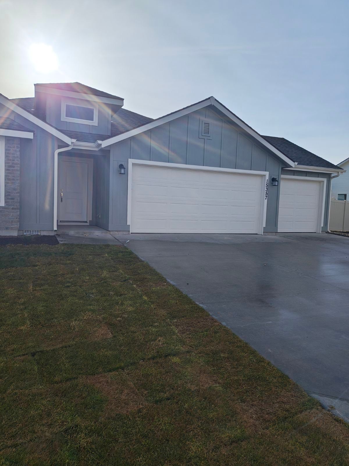 Blue house with white garage doors and a wet driveway.