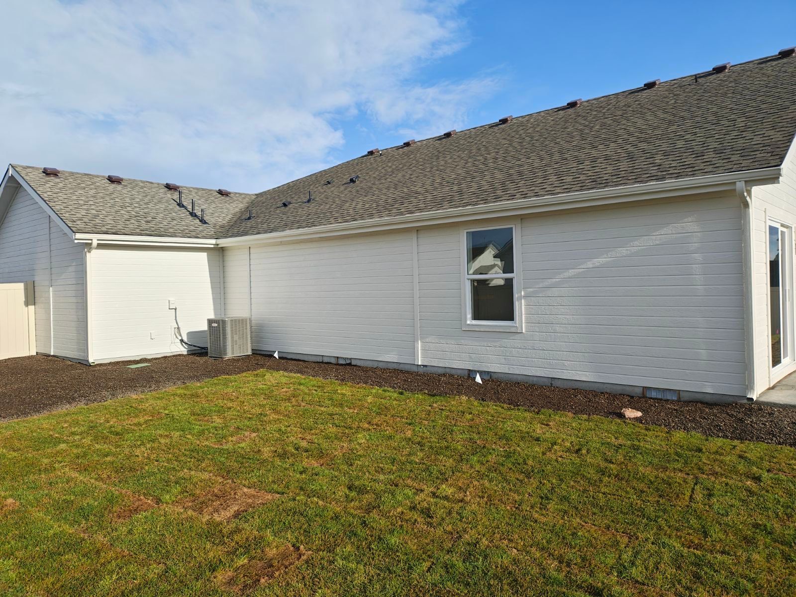 Side view of a white house with a dark gray roof, green lawn, and blue sky.