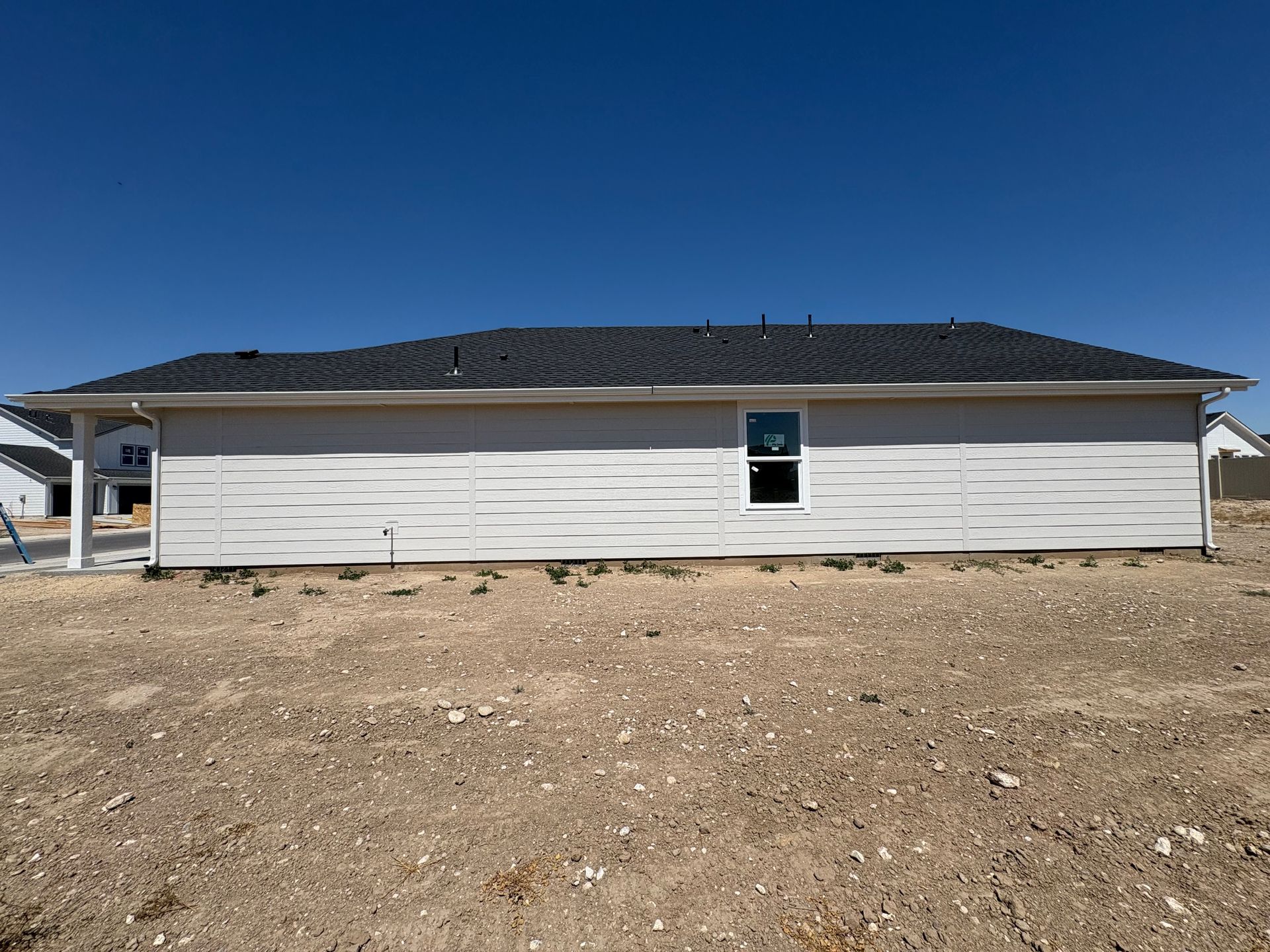 Side view of a light-colored house with a dark roof on a sunny day. A small window is centered.