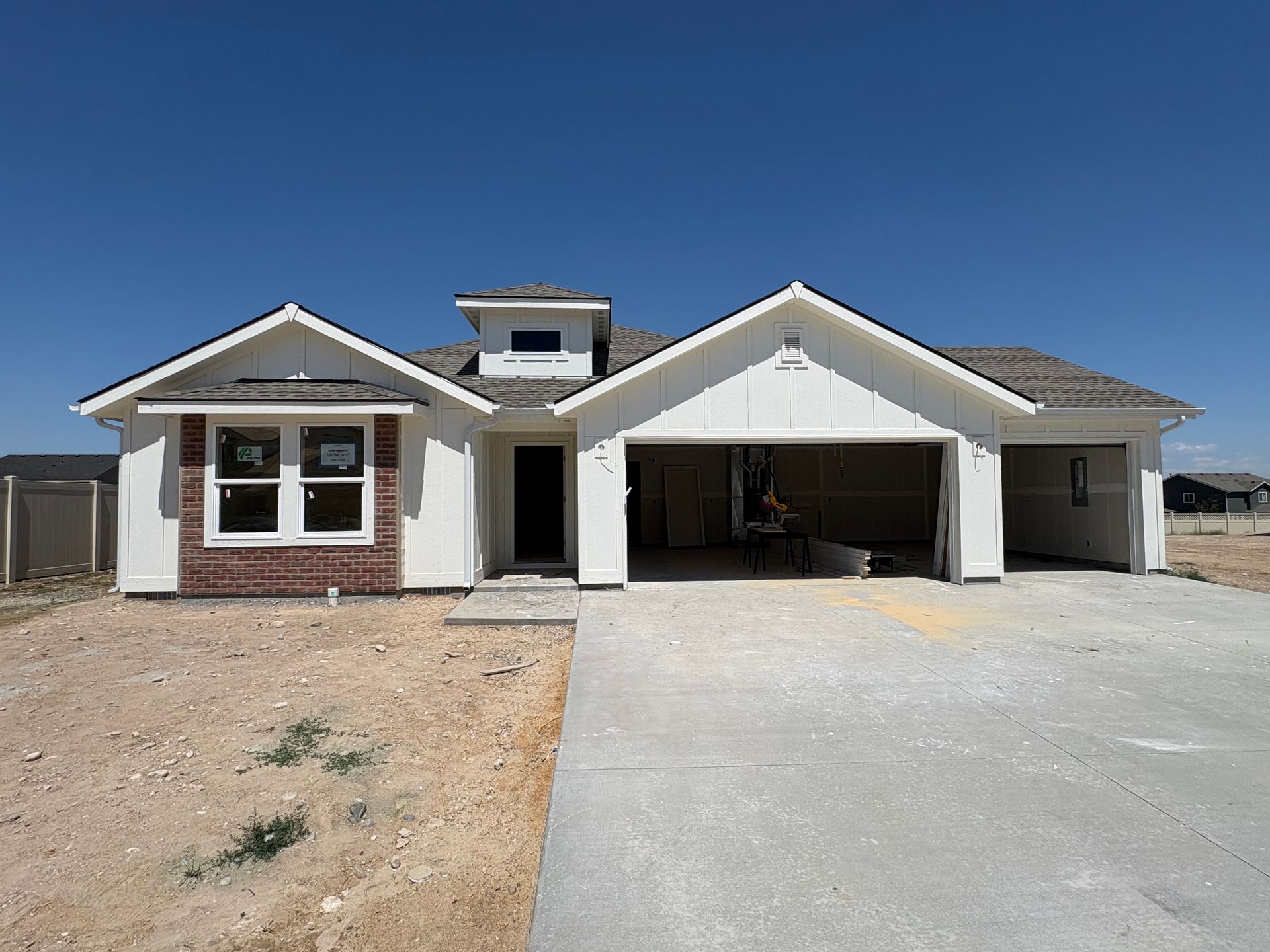 New construction house, white siding, brick accents, two-car garage, concrete driveway, blue sky.