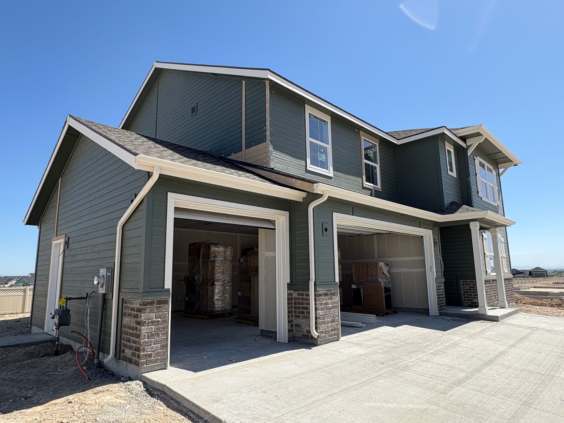 New house under construction with green siding, open garage doors, and stone columns, under a clear blue sky.