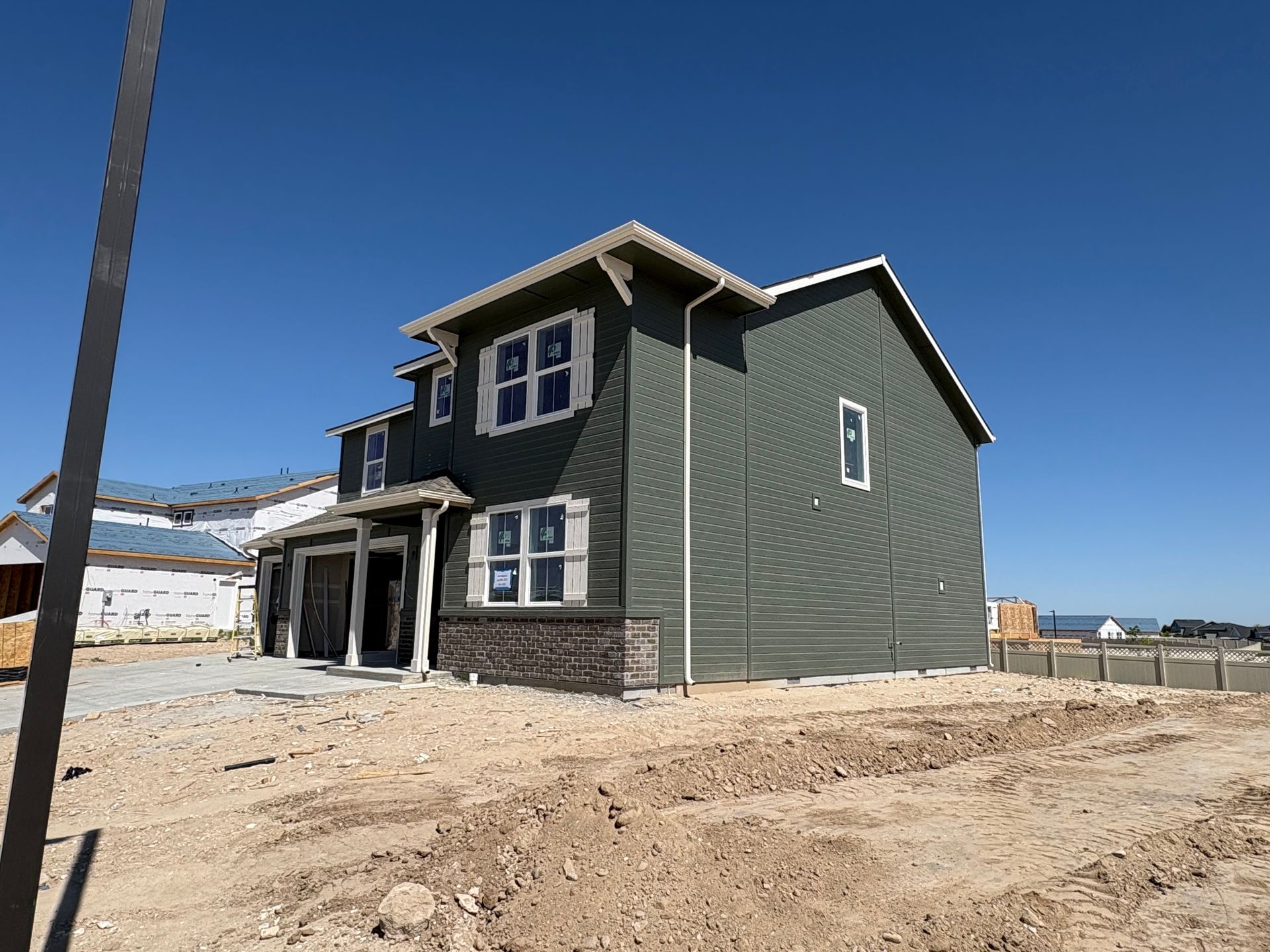 New house under construction with green siding, on a dirt lot, against a blue sky.