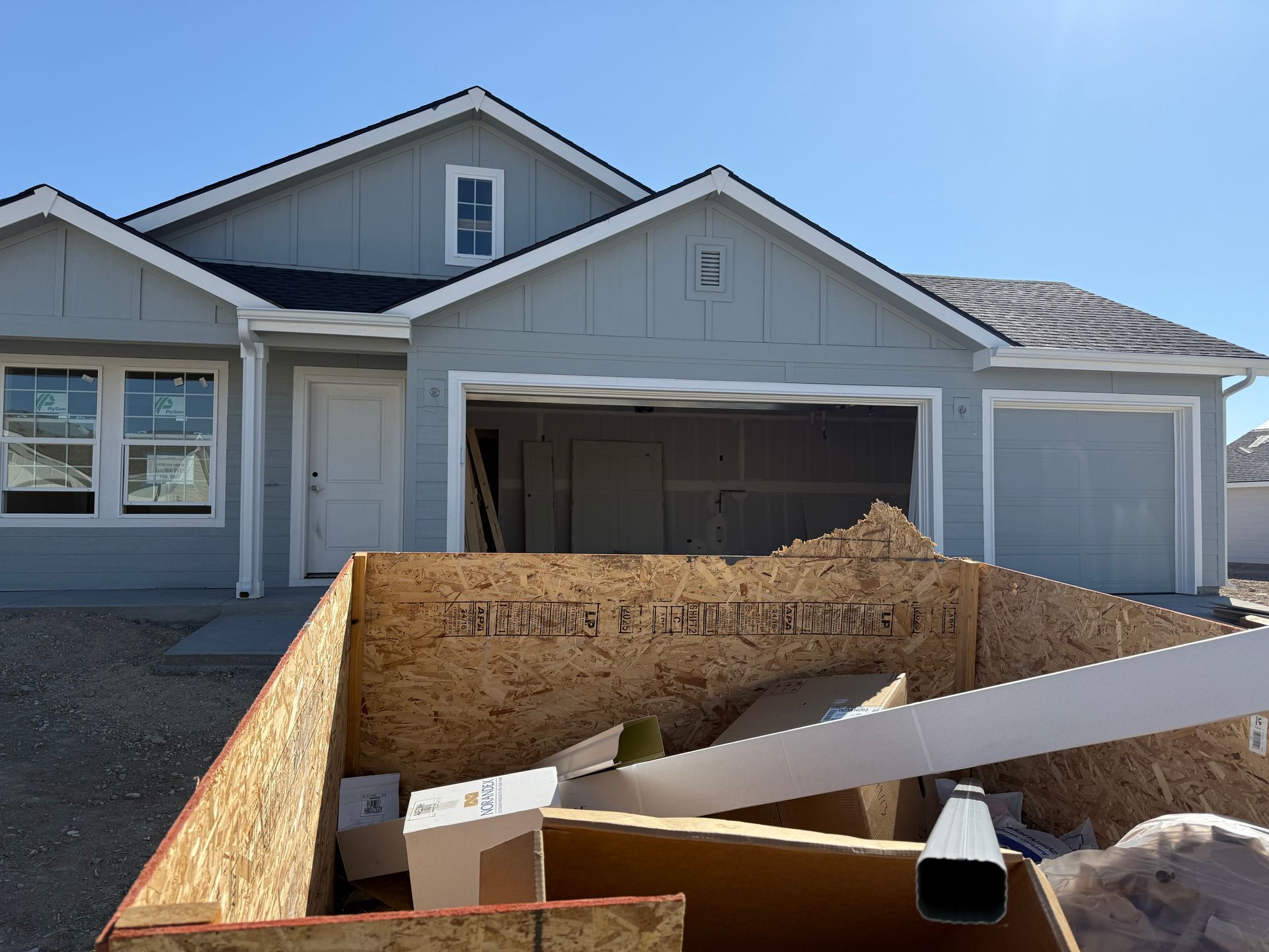 Construction dumpster in front of a light blue house with open garage doors.