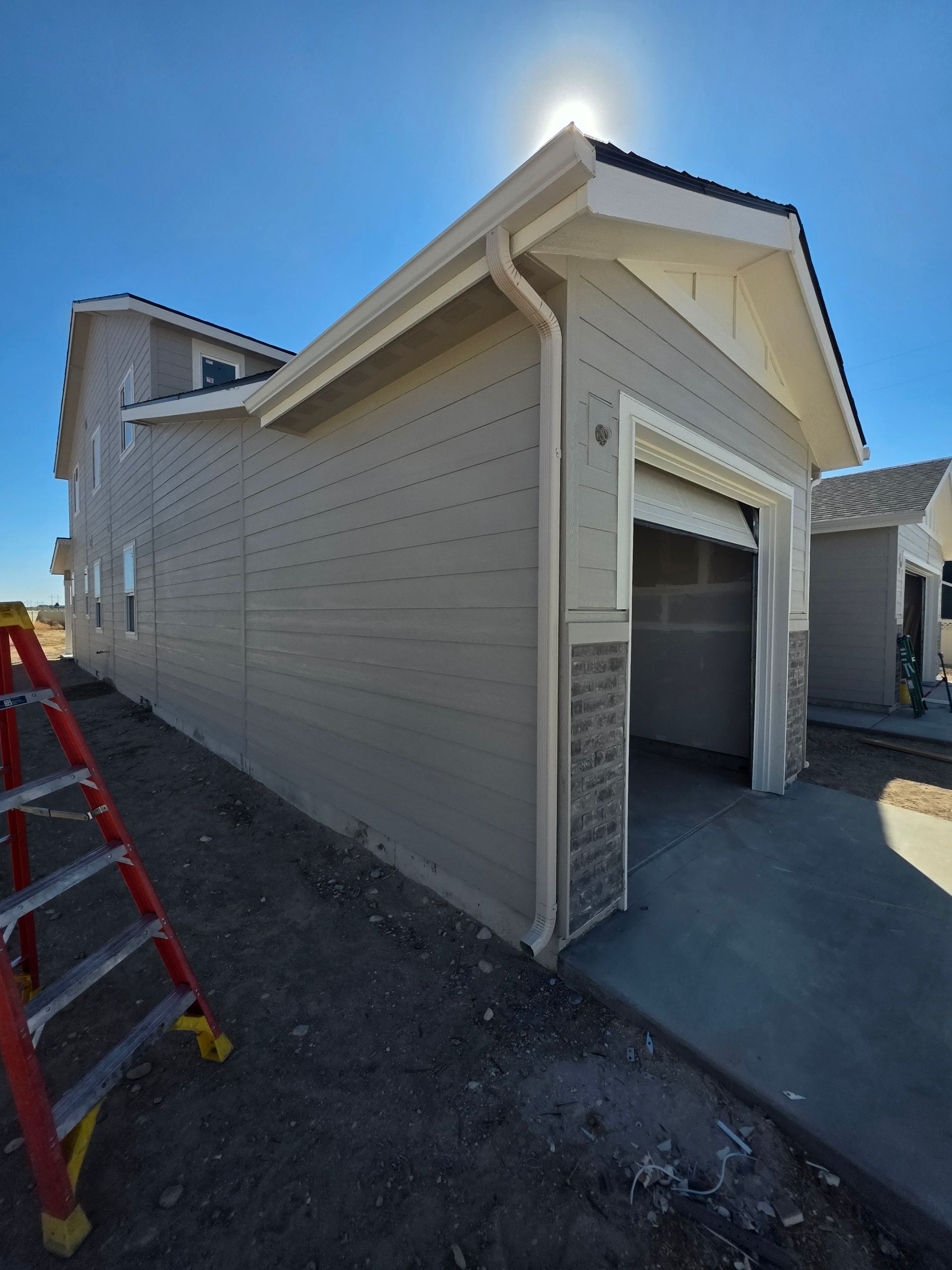 Exterior of a beige house with an open garage door and a ladder on the side, under a sunny sky.
