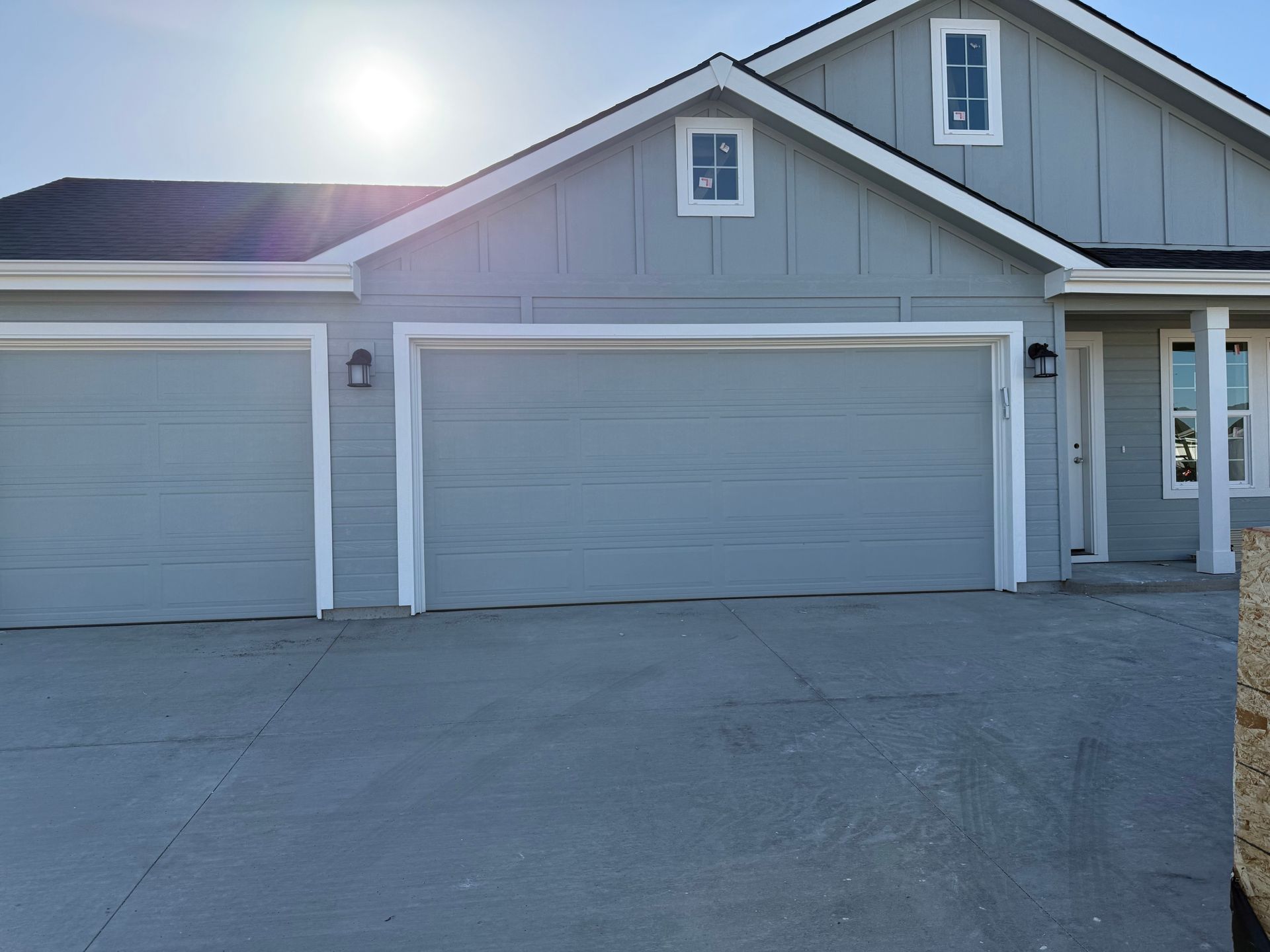 Light blue house with two garage doors and a concrete driveway on a sunny day.