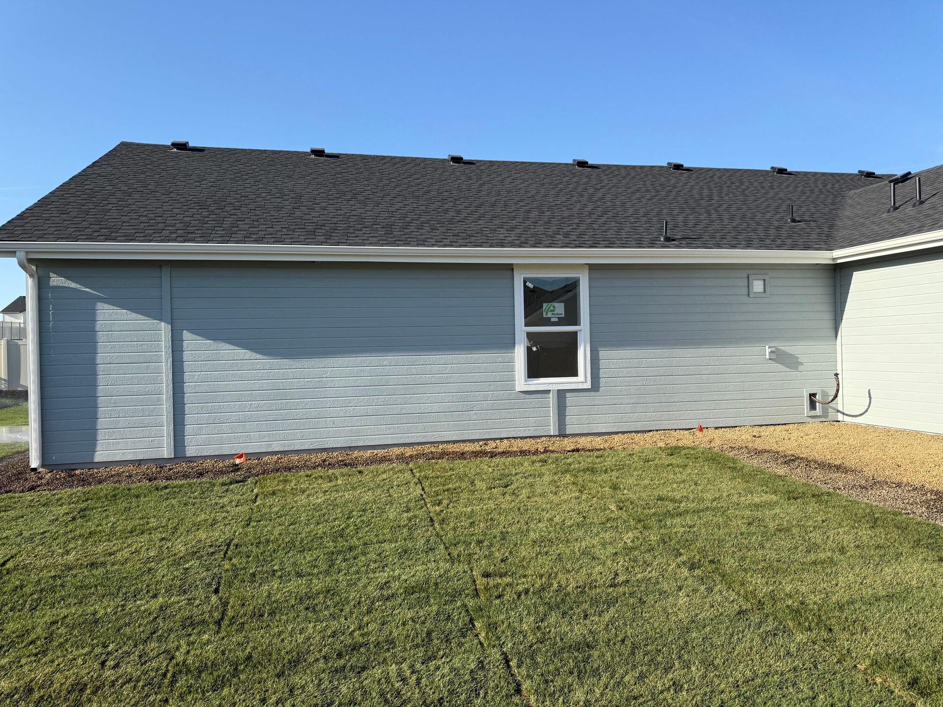 Side of a house with light blue siding, a small window, and a dark gray roof. Green grass and blue sky.
