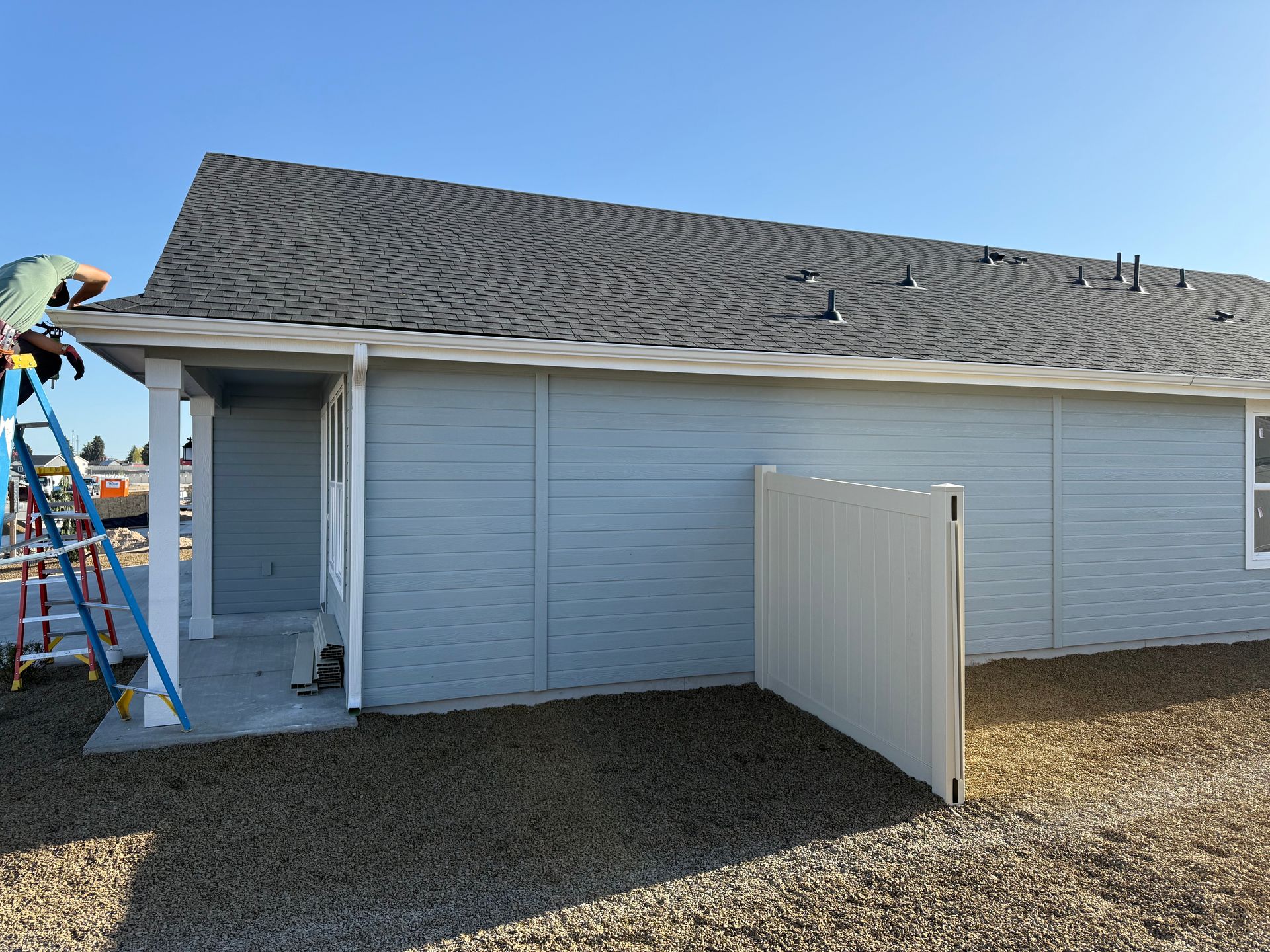 Exterior of a light blue house under construction with a person on a ladder working on the roof.