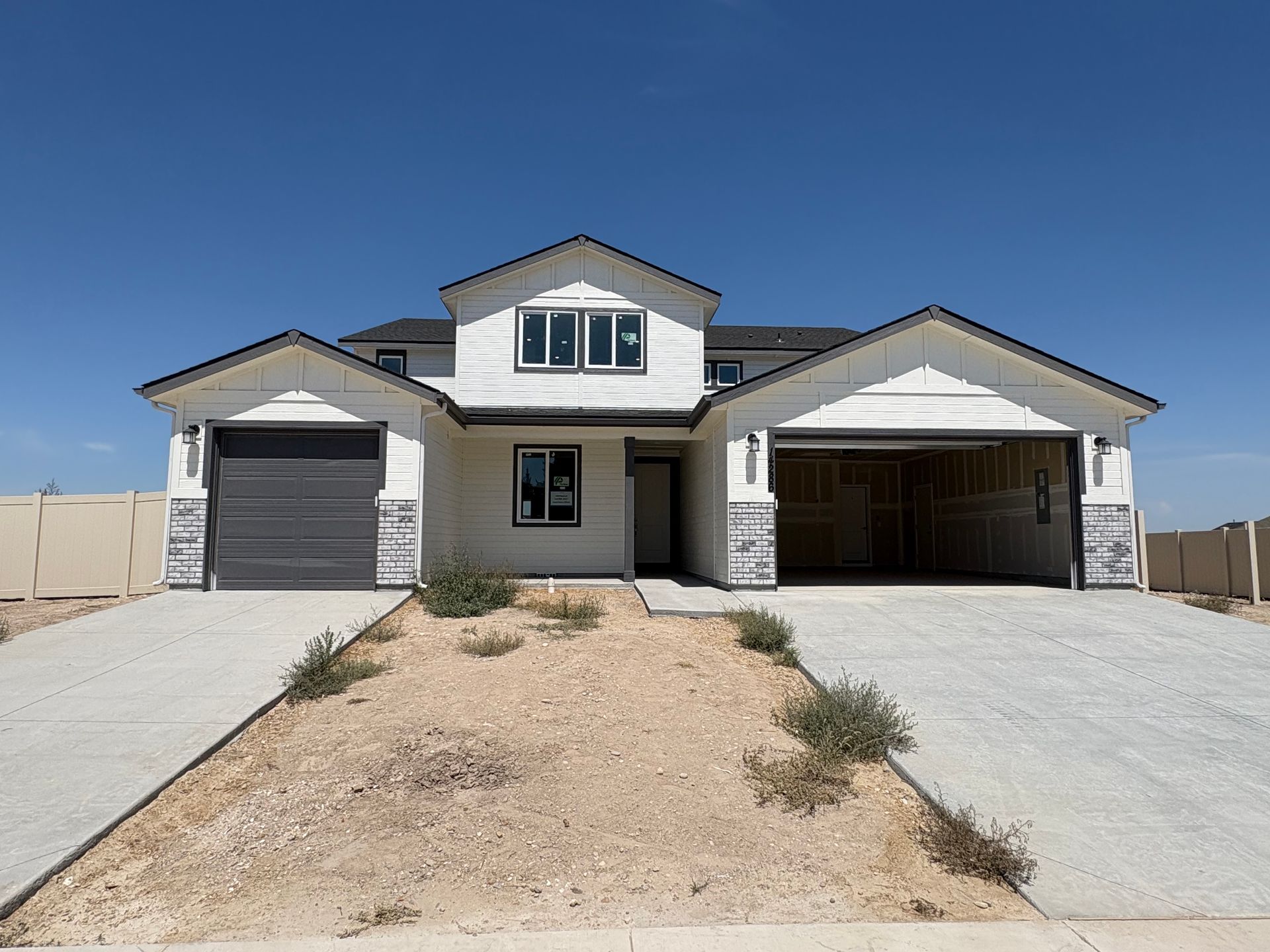 Two-story white house with gray garage doors and unfinished landscaping. Blue sky.