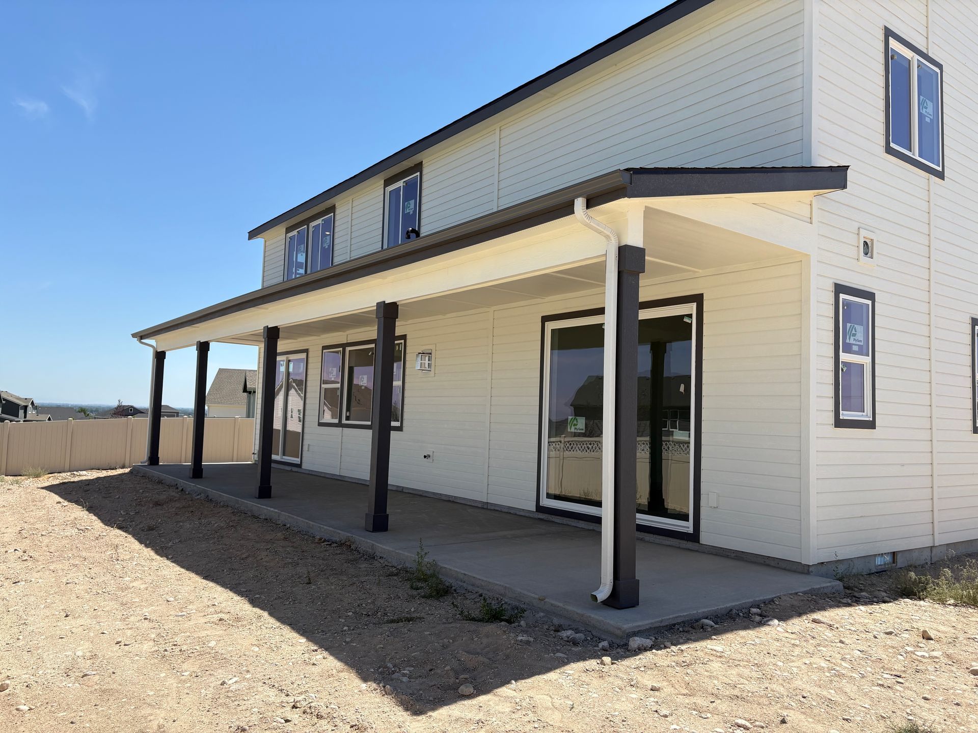 Two-story house with a long, covered patio. Tan siding, dark trim, and a concrete patio.