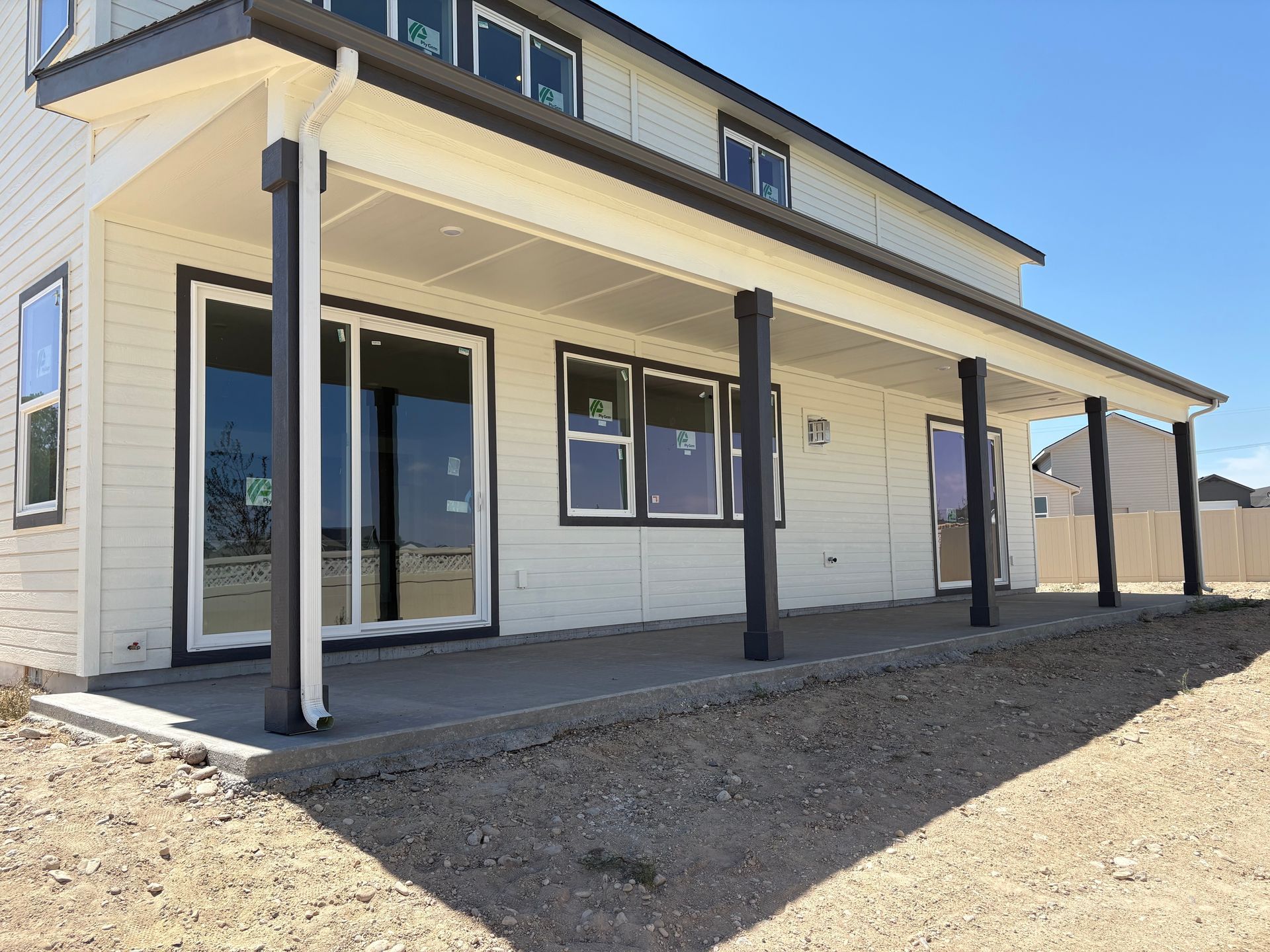 Backyard view of a two-story house with a covered patio, columns, and a concrete floor. Gravel in the foreground.