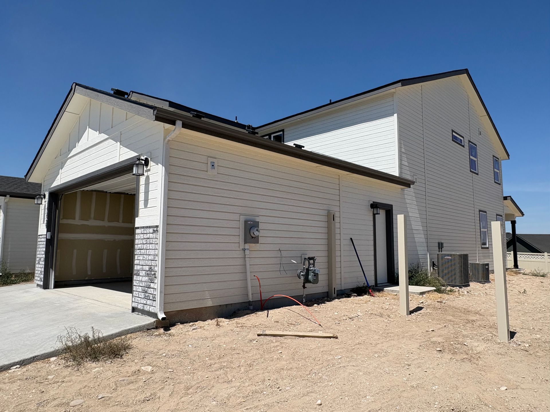 White two-story house under construction with an attached garage; open garage door, siding, and clear blue sky.