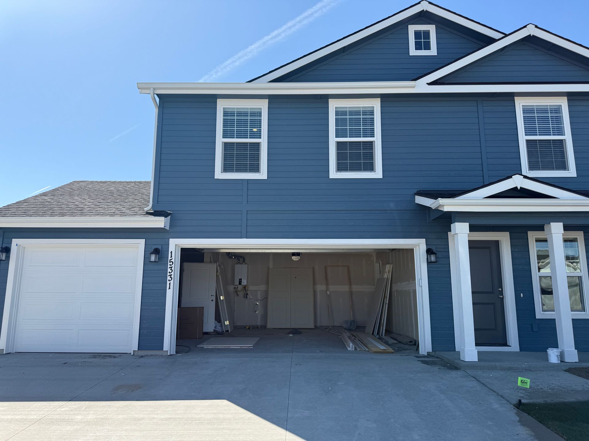 Blue house with white trim, a partially open garage, and a concrete driveway on a sunny day.