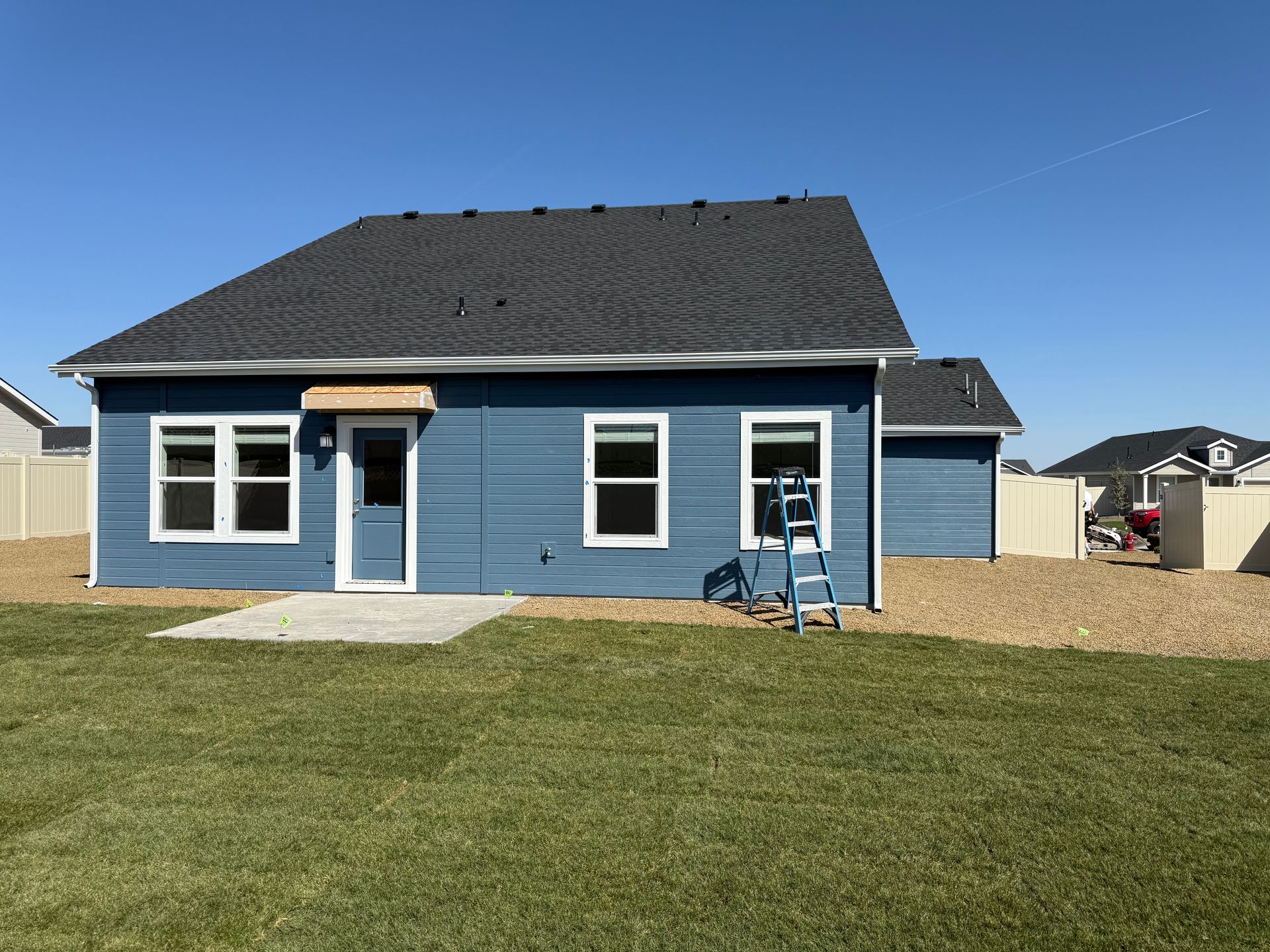 Blue house with white trim and gray roof. Backyard with lawn and gravel.