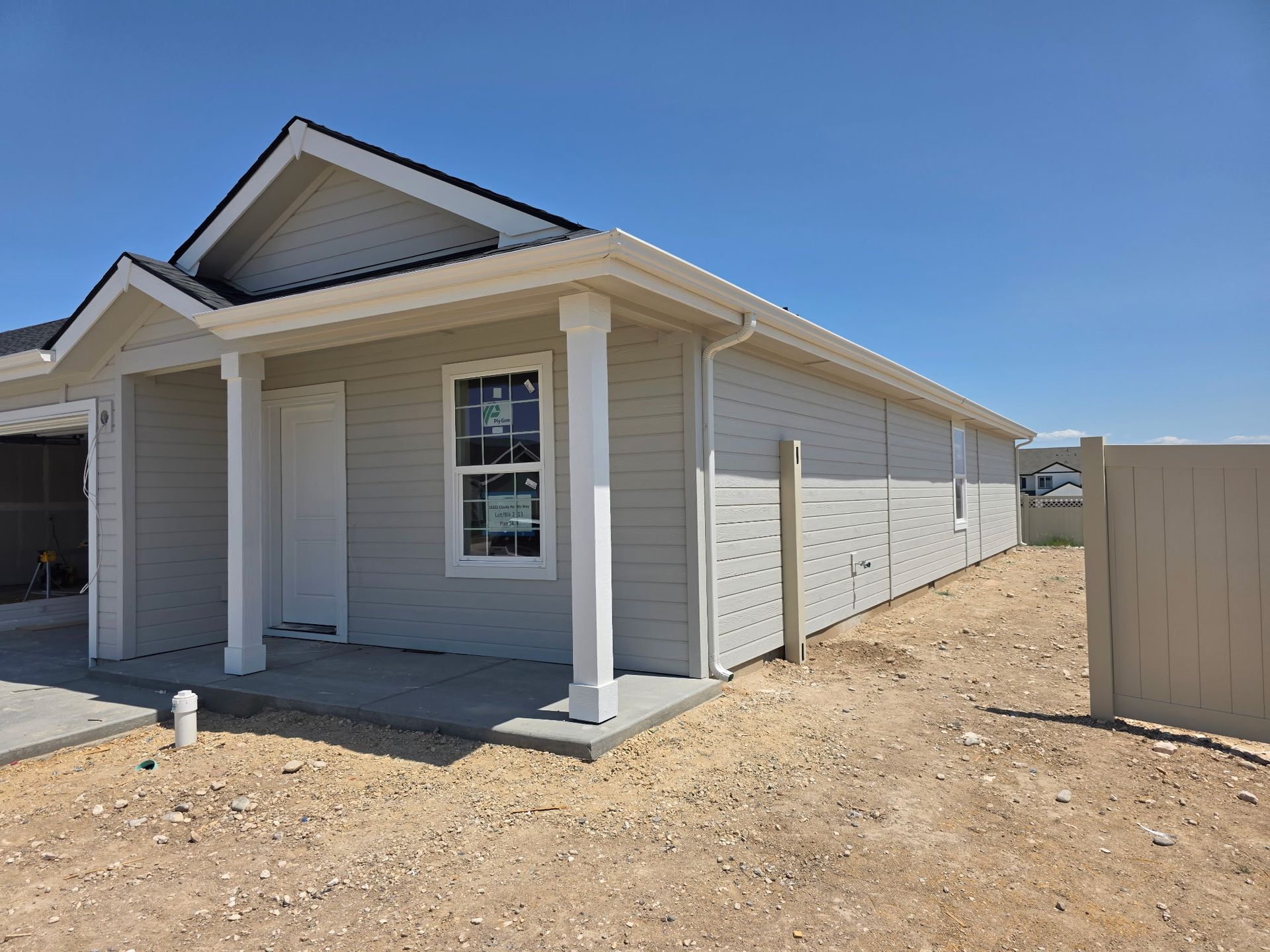 New light gray house with white trim, a concrete porch, and a fence, under a blue sky.