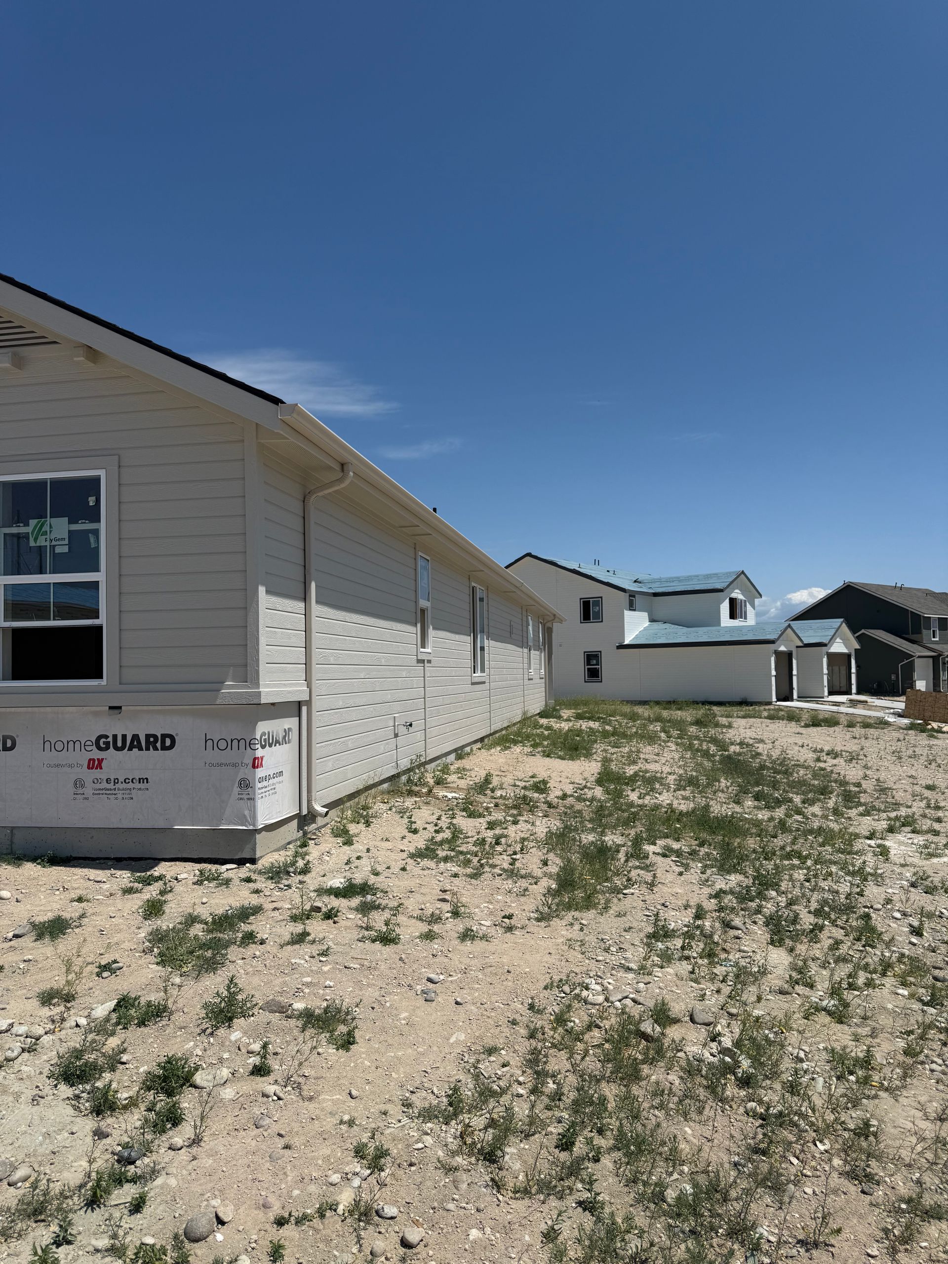 New homes under construction; beige siding, blue sky, and patchy grass.