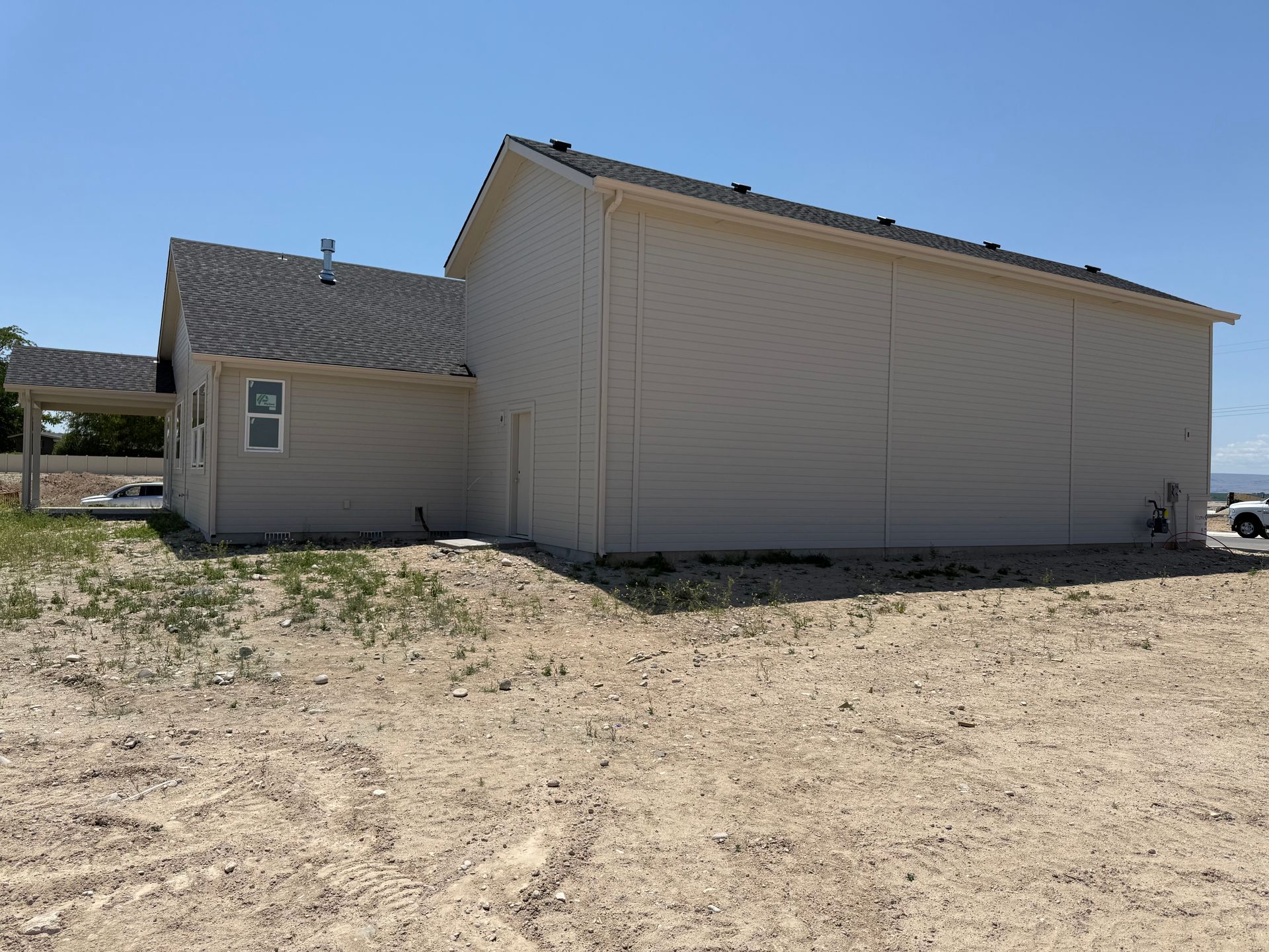 Tan house with gray roof on a dirt lot under a clear sky.
