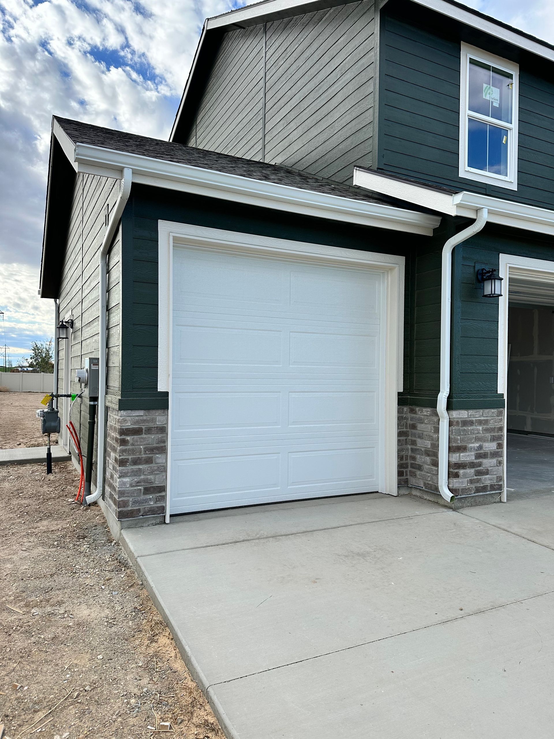 Exterior of a two-story house with a white garage door and dark teal siding.