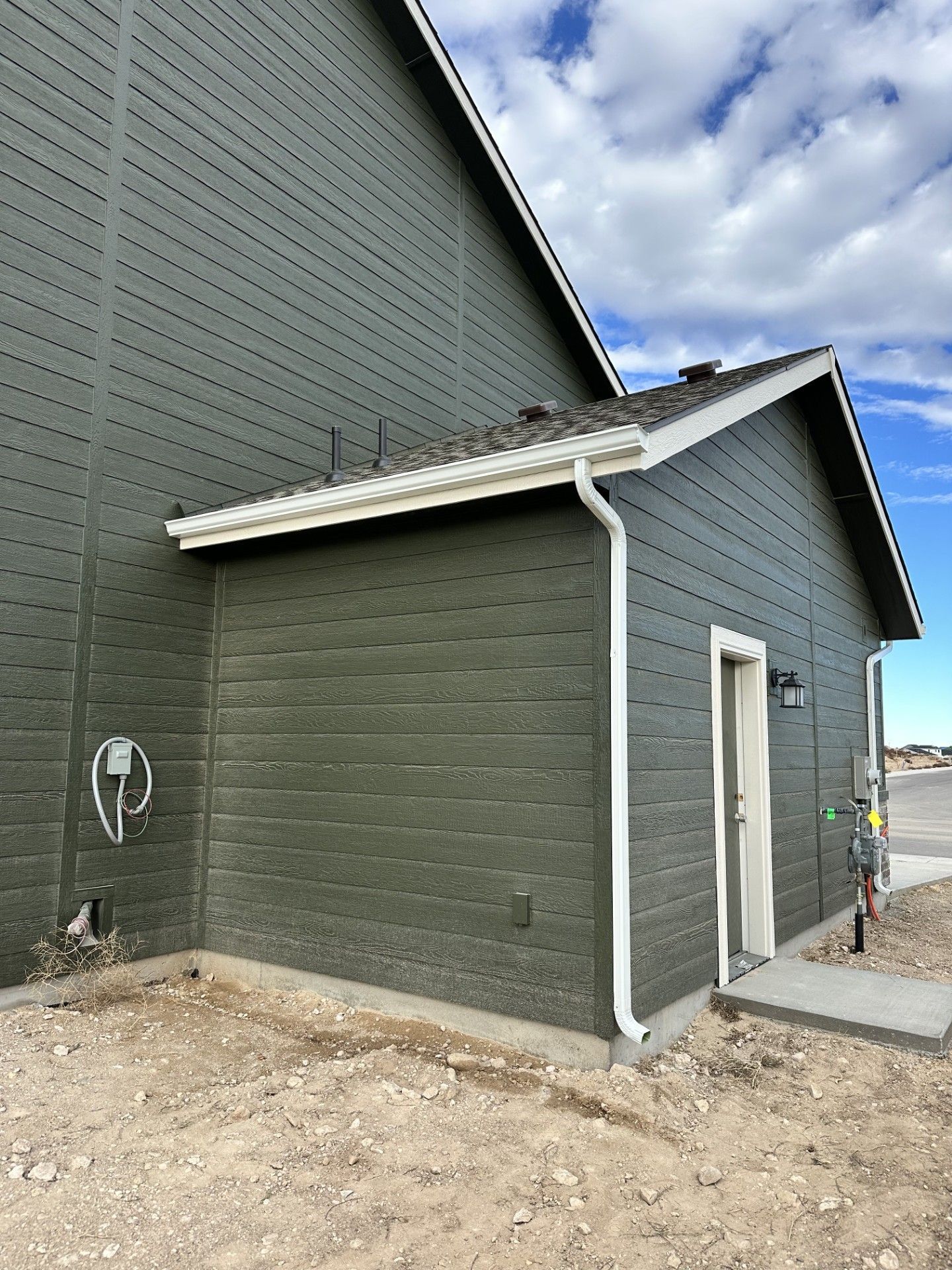 Green building exterior with white trim, downspout, and door.