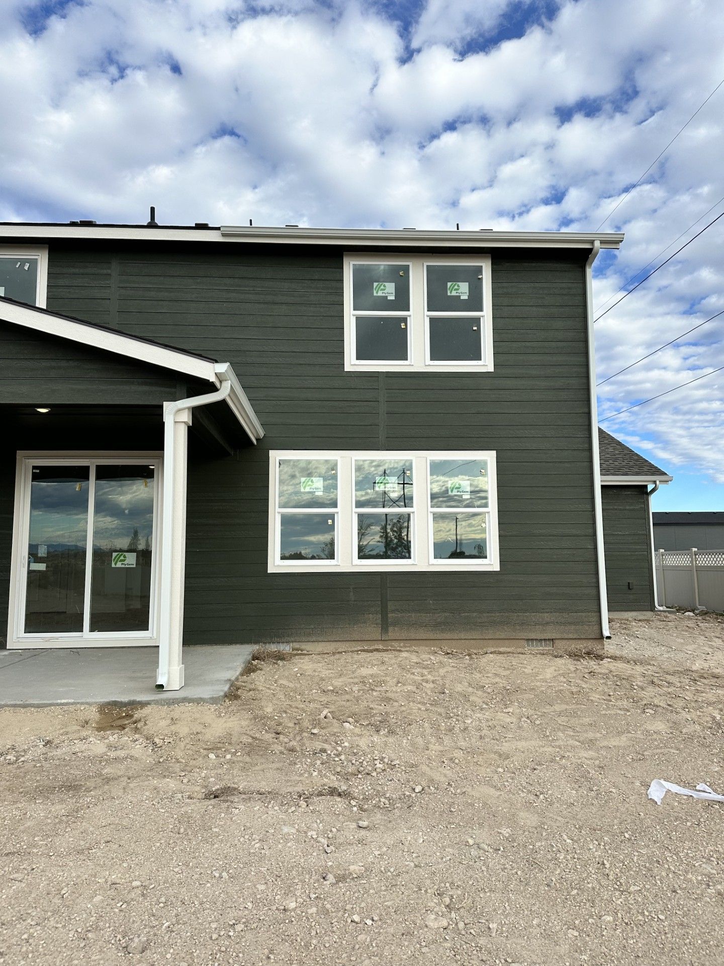 Dark green house with white-framed windows, under construction, against a cloudy sky.