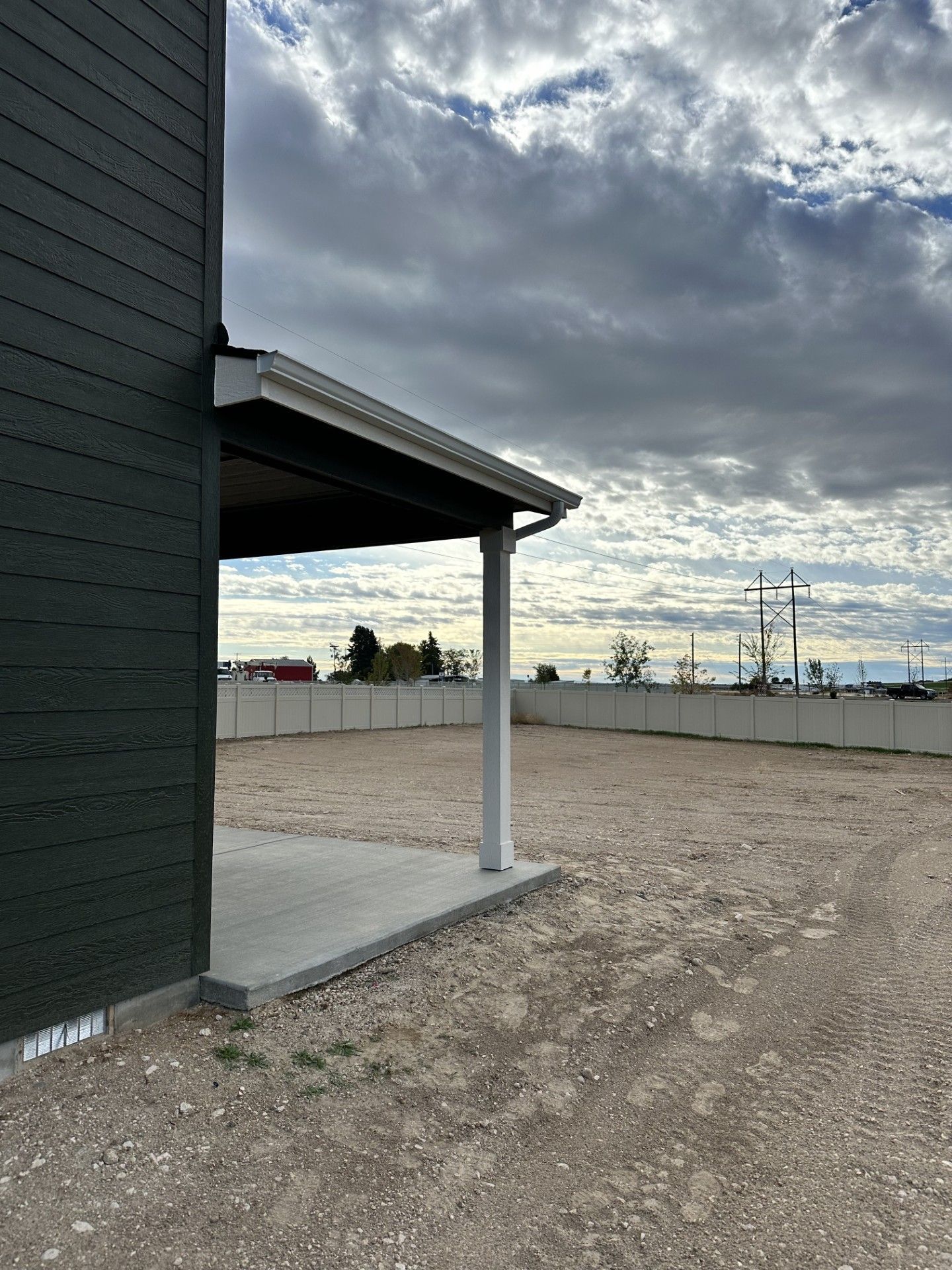 Dark green house exterior with a covered patio, gravel, and cloudy sky.