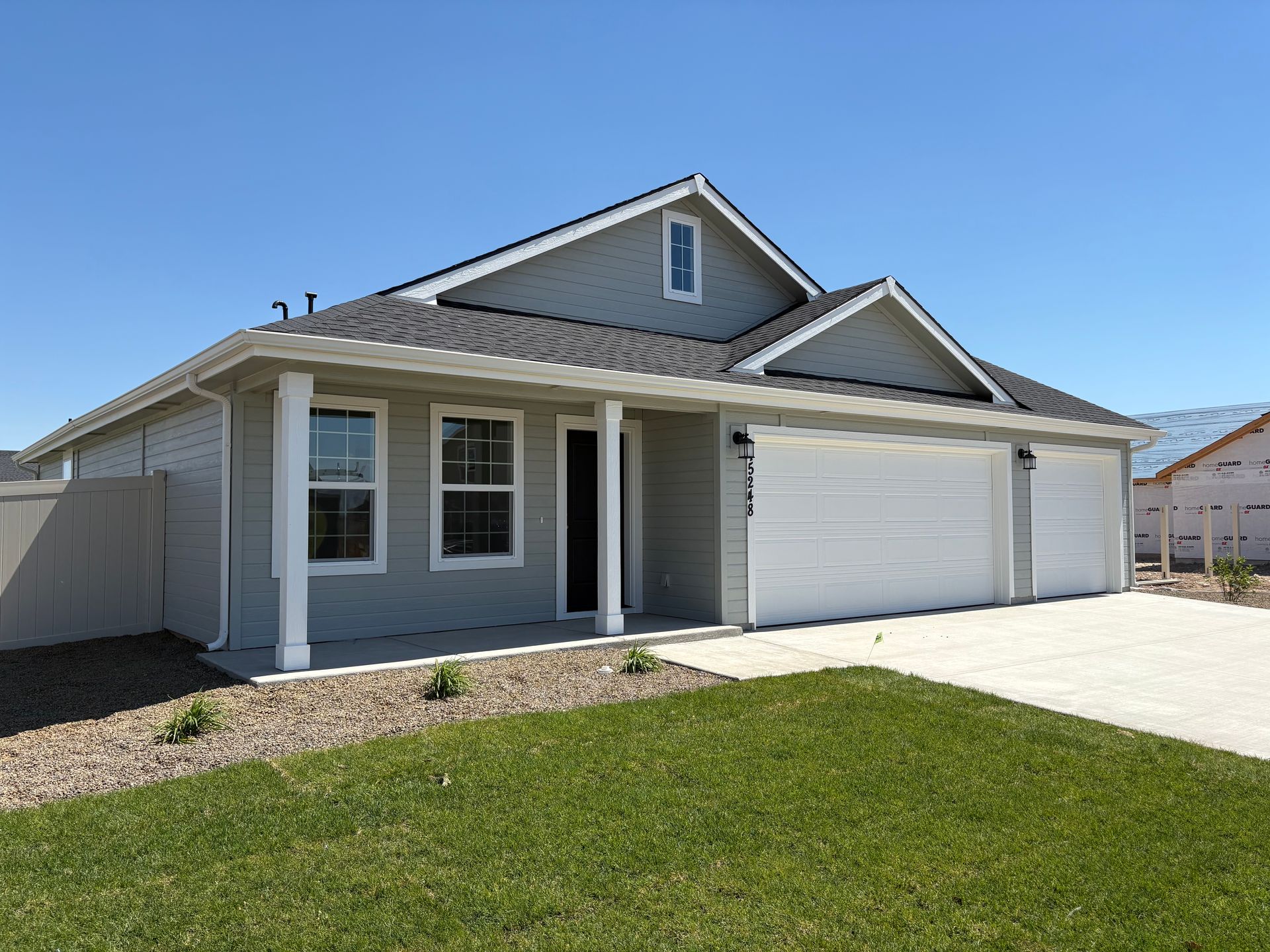 Gray house with white garage doors and a green lawn under a blue sky.