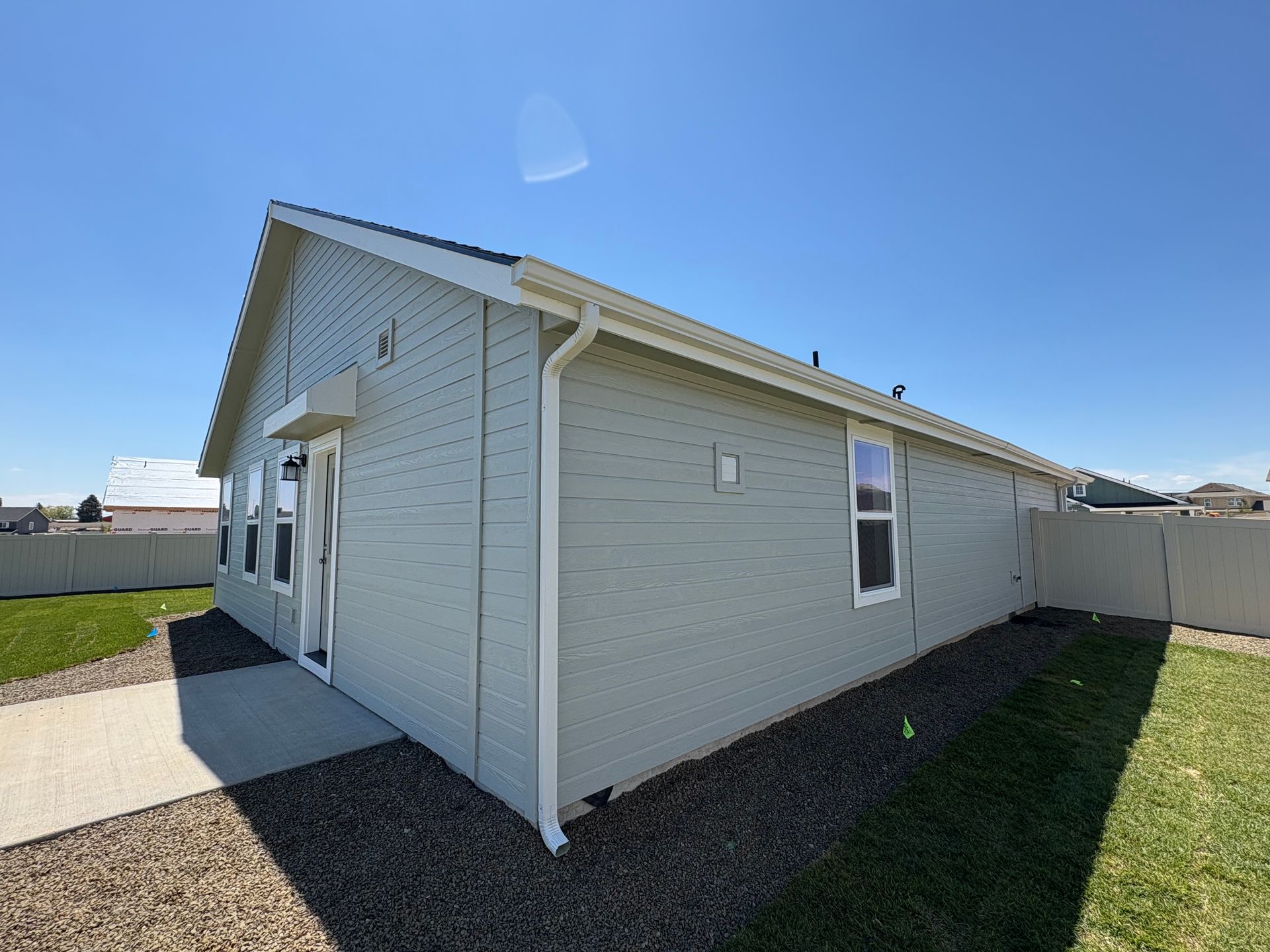 Side view of a light green house with white trim, gutters, and a blue sky.
