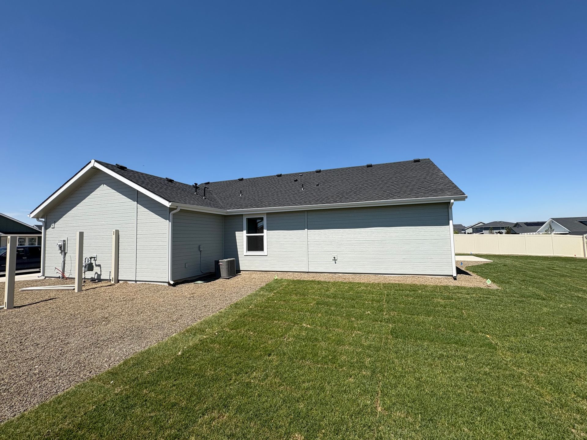 Light blue house with dark roof, small window, and gravel path on a sunny day.