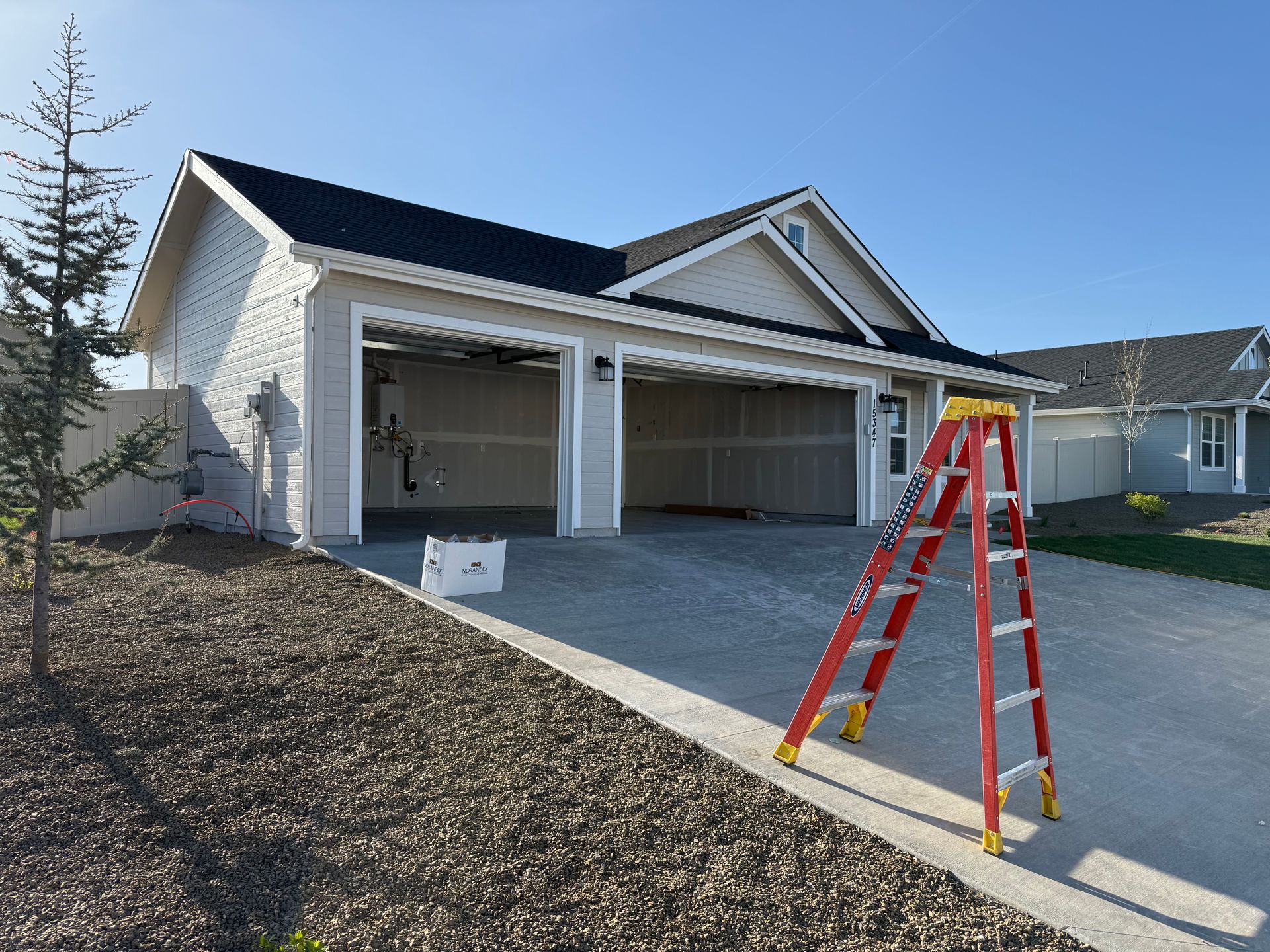 Garage with open doors, concrete driveway, red ladder, and landscaping.