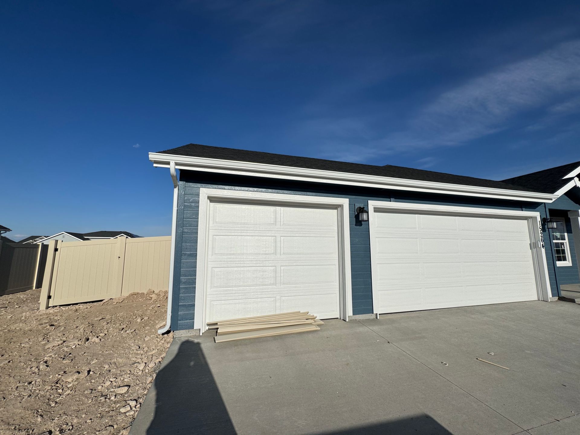 Blue garage with two white doors, concrete driveway, and tan fence.
