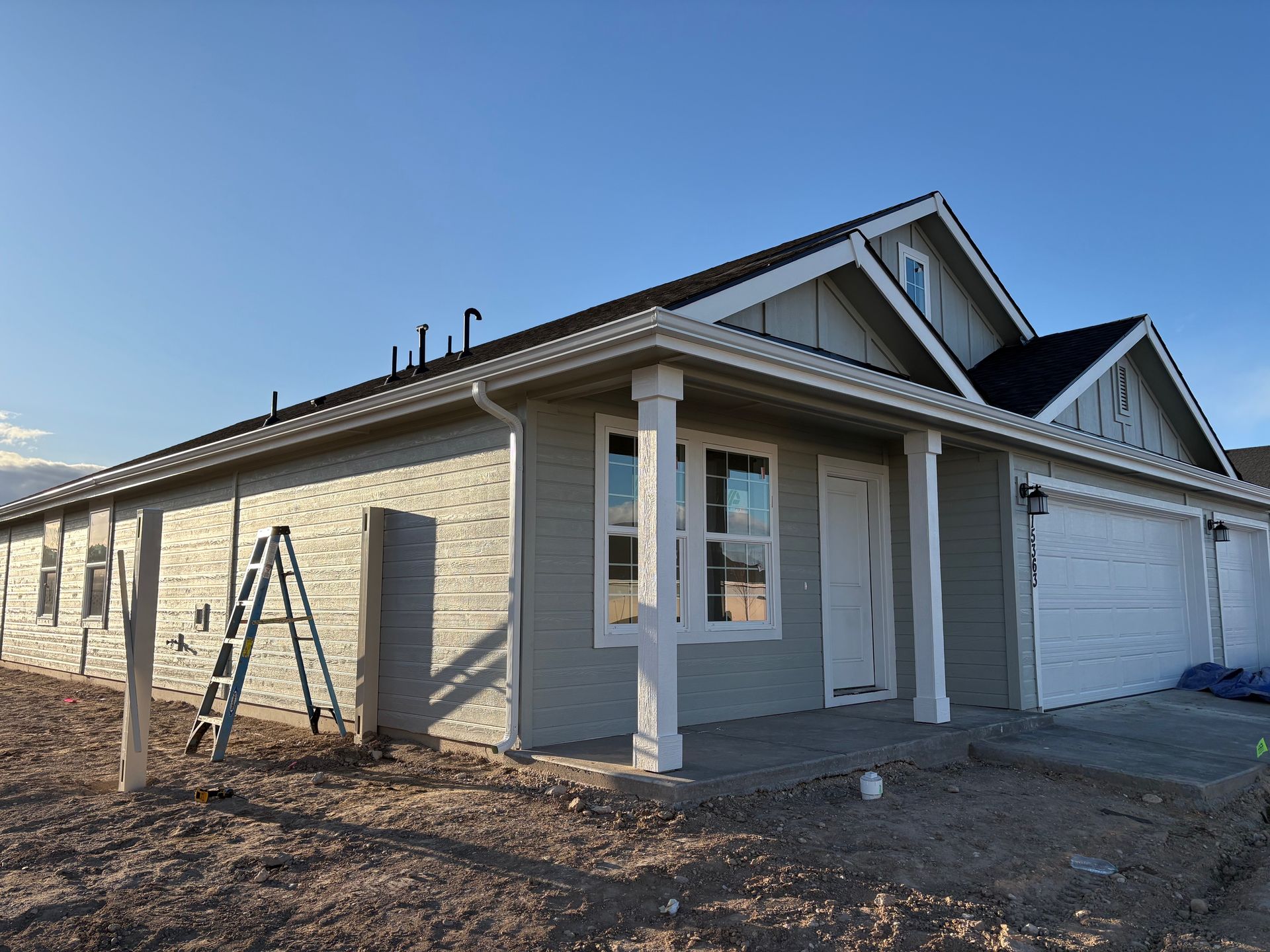 New house under construction, gray siding, white trim, garage, blue sky, ladder.