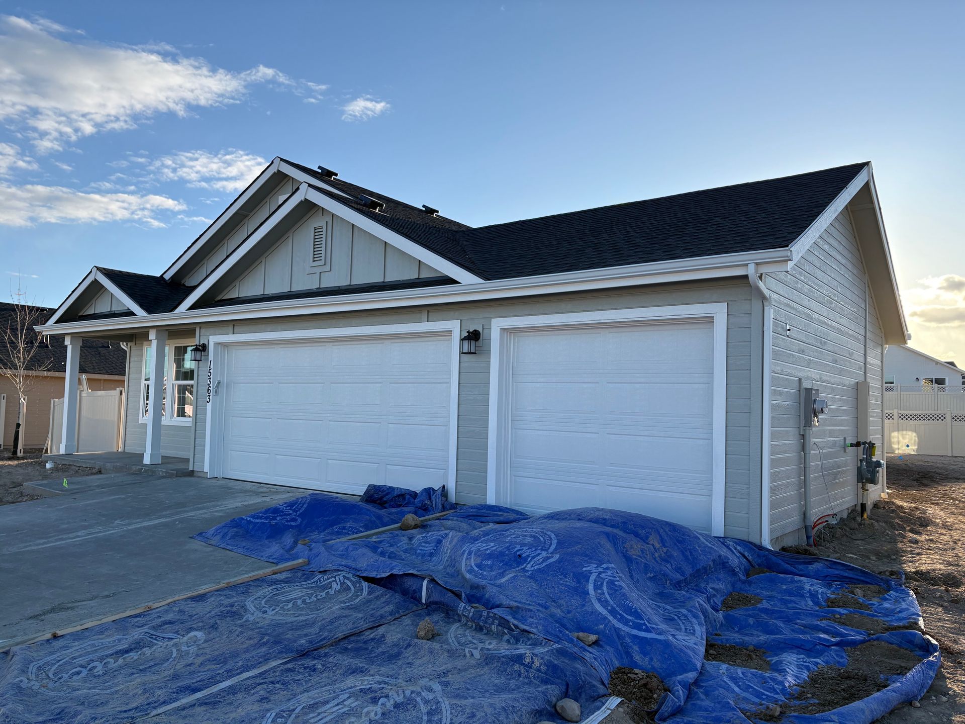 New house under construction with white garage doors and blue tarp in front.