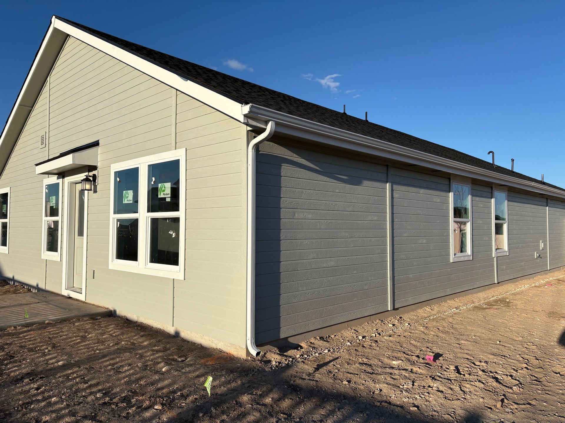 A new, light gray house under construction with white-framed windows, against a blue sky.