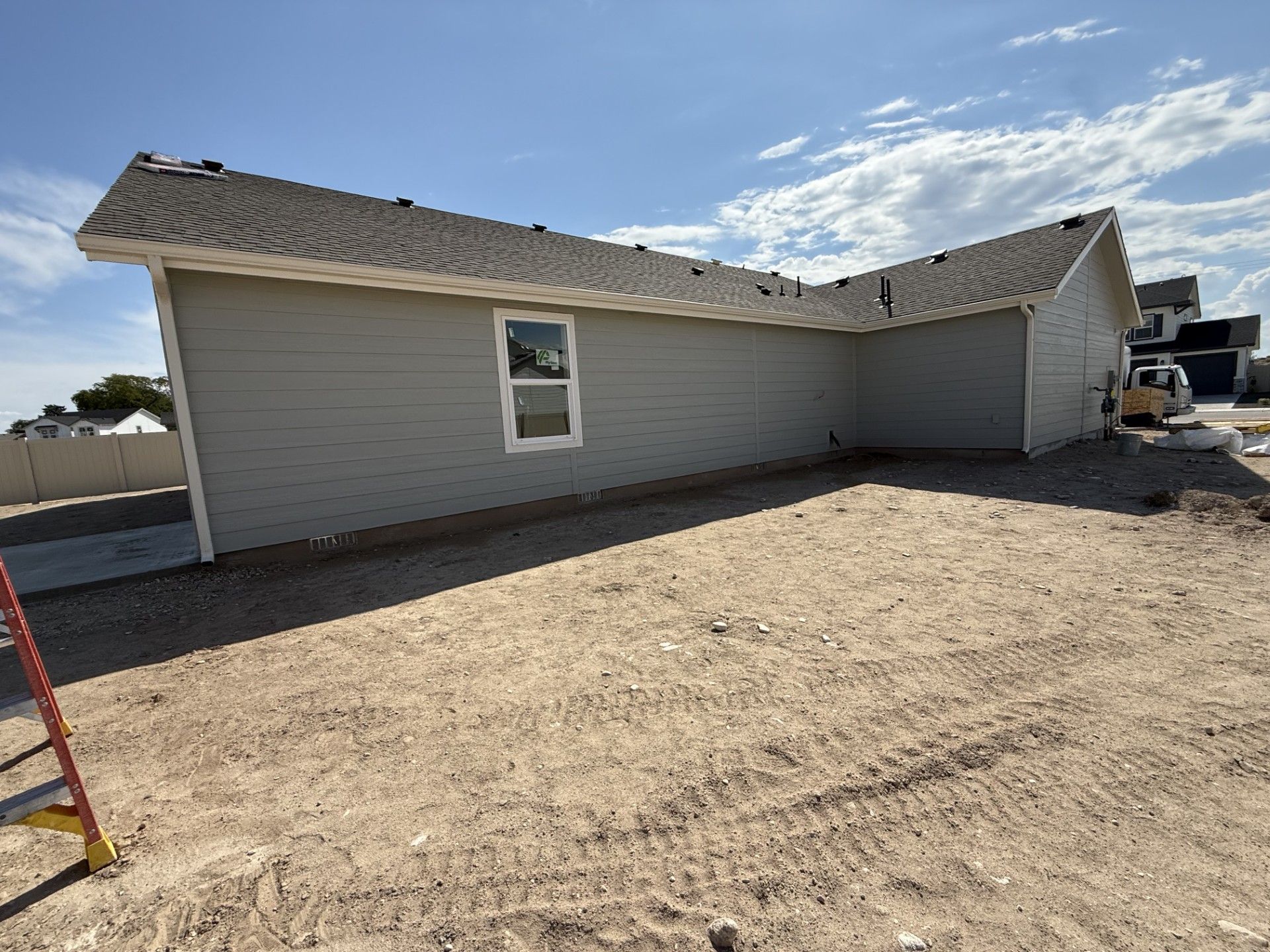 Side view of a light gray house under construction, with a window and a bare yard.