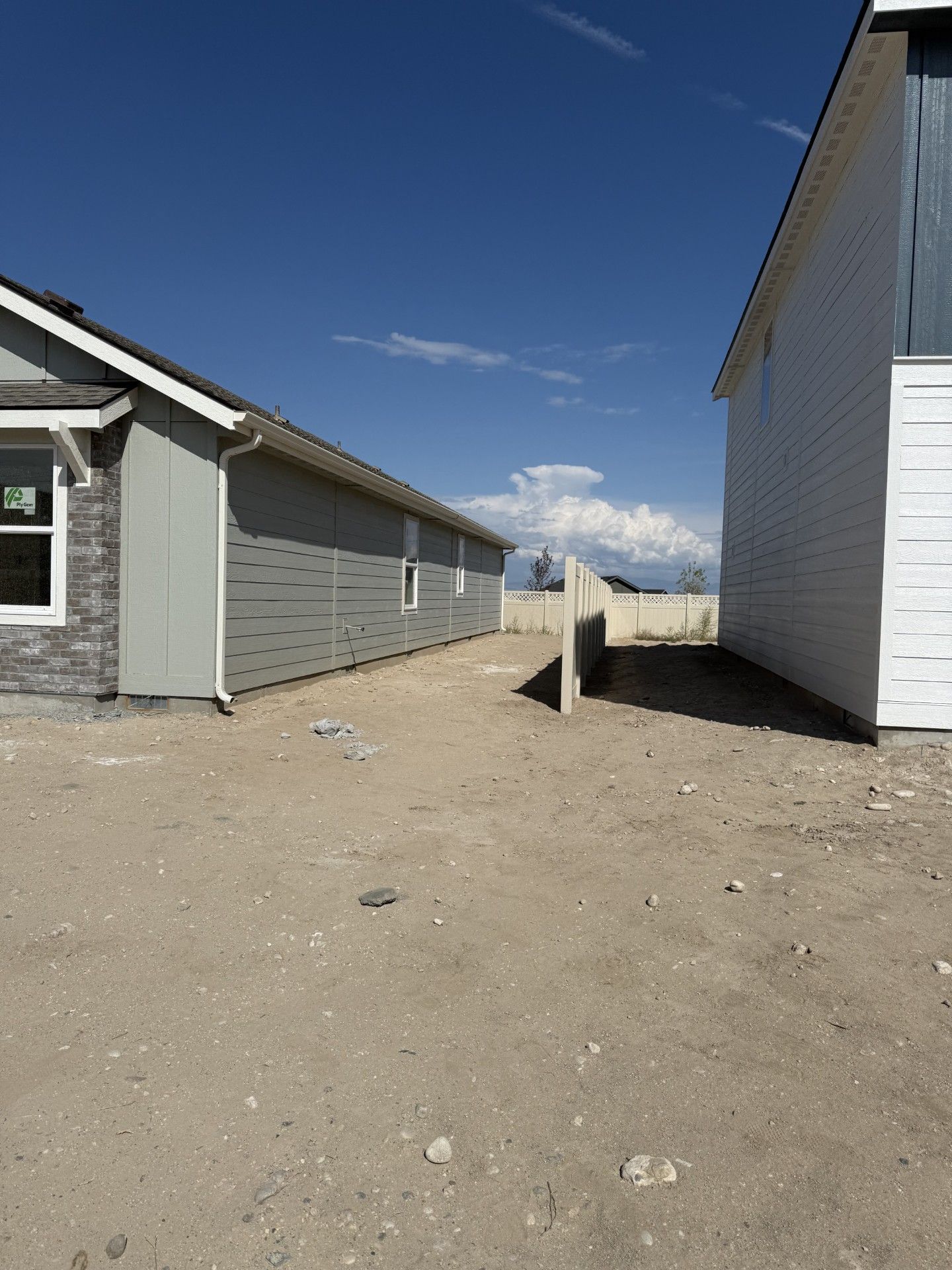 Two houses under construction with a dirt lot in between, under a blue sky.