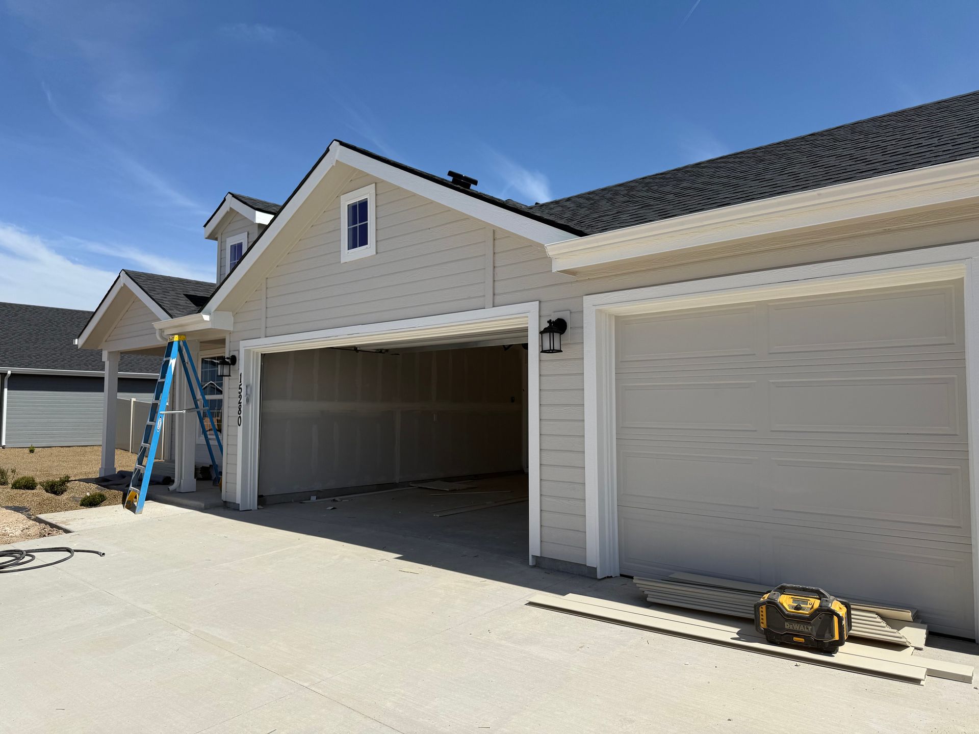 Beige house with open garage doors; blue sky in background. Construction materials are visible.