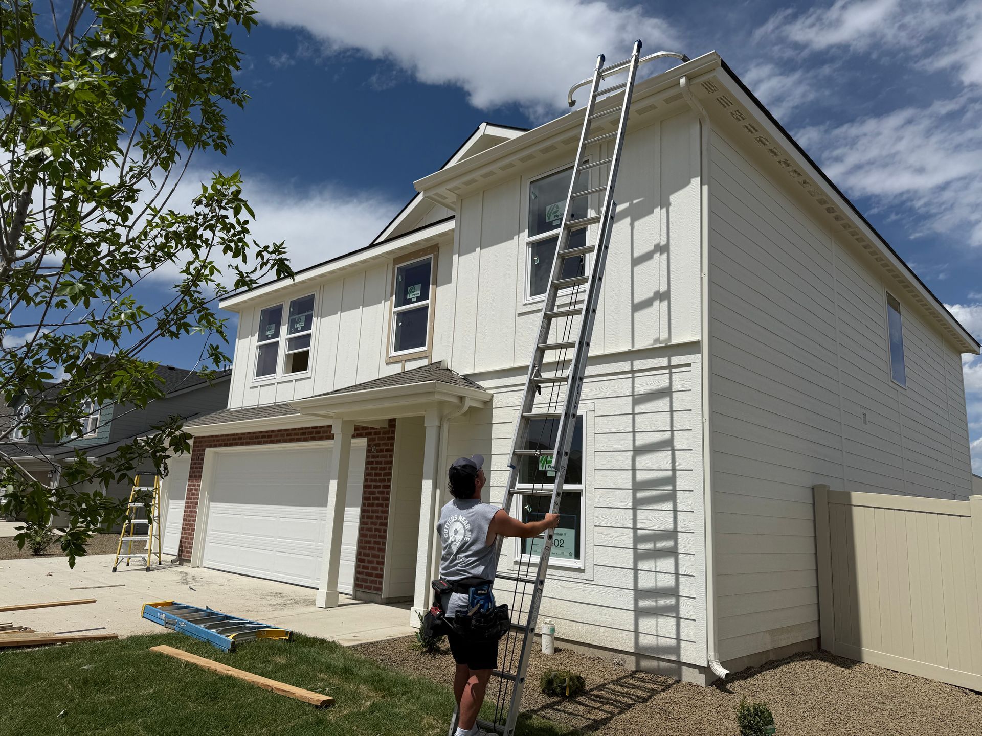 Person on ladder by a white house, working on the roof under a blue sky.