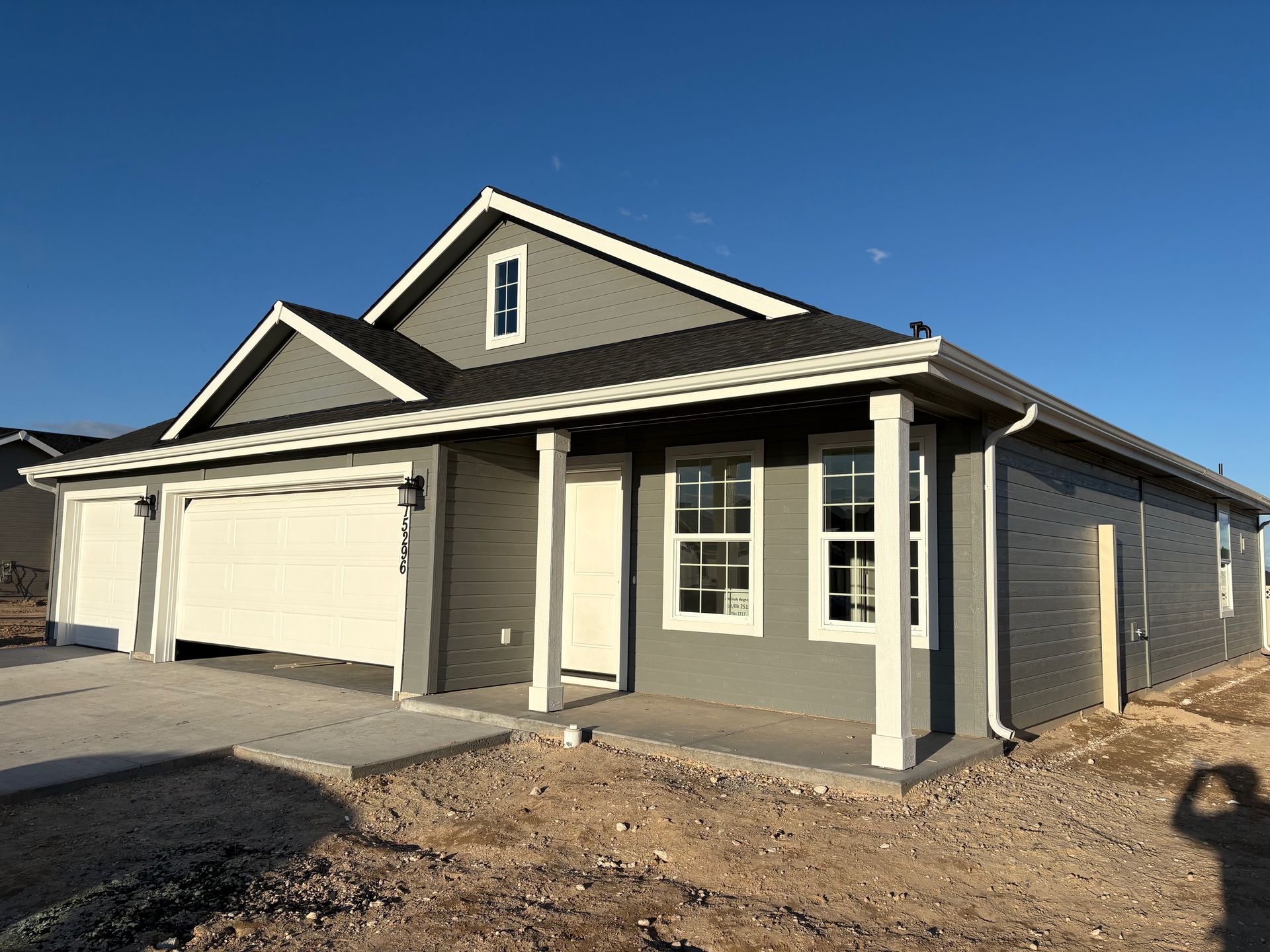 Gray house with white trim, a two-car garage, and a concrete walkway under a clear, blue sky.