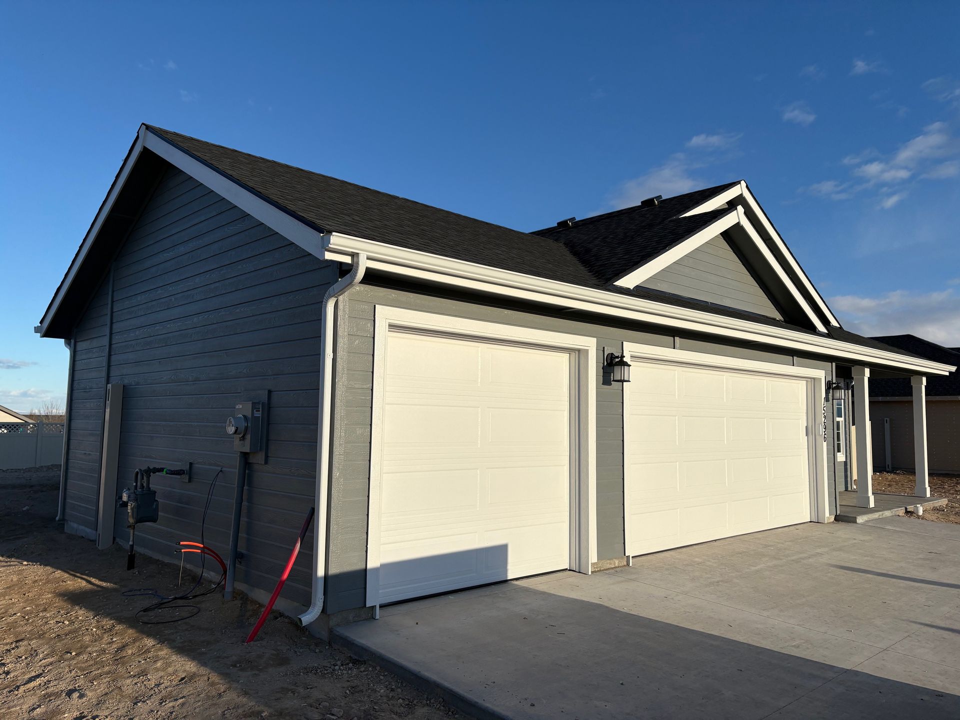 Gray house with white garage doors, a dark roof, and blue sky.