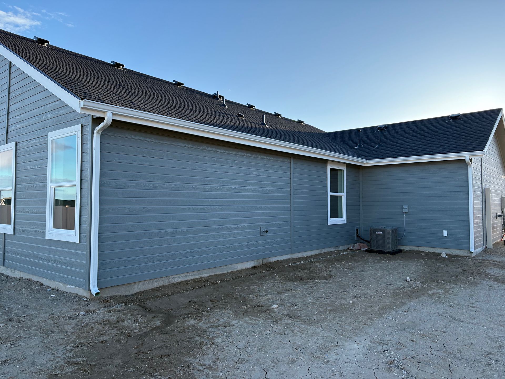 Gray siding on a new house with white trim, gutters, and windows against a blue sky.