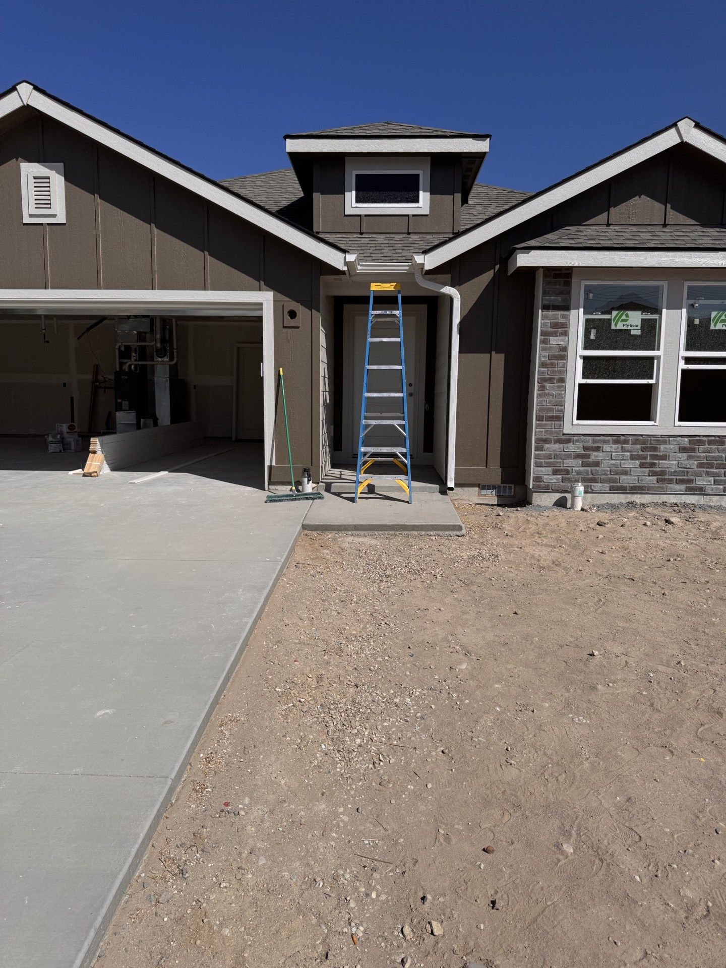 New house exterior under construction, ladder in front of doorway, gravel and concrete.