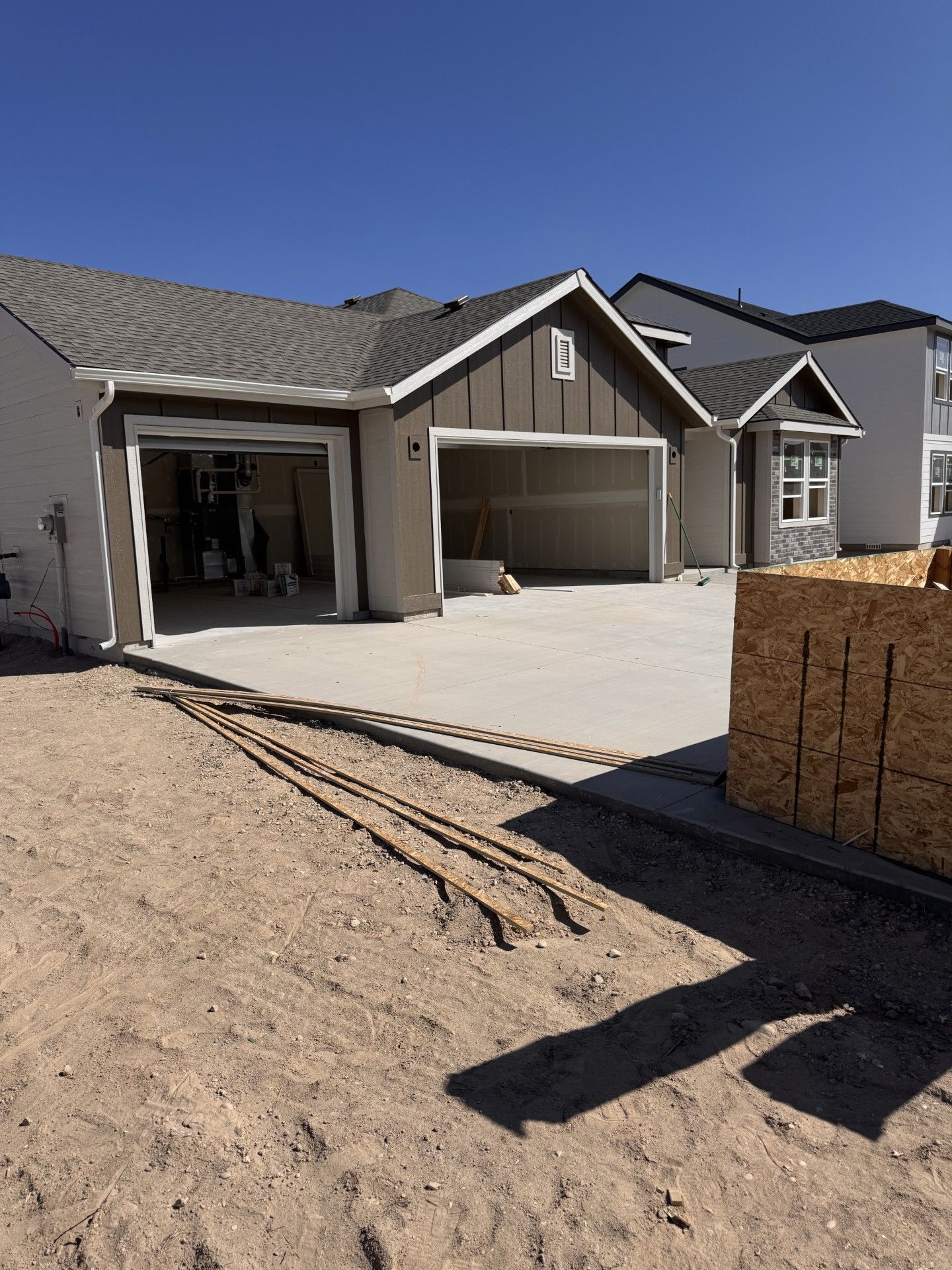 New house with open garage doors and concrete driveway, in a sunny setting with exposed dirt.