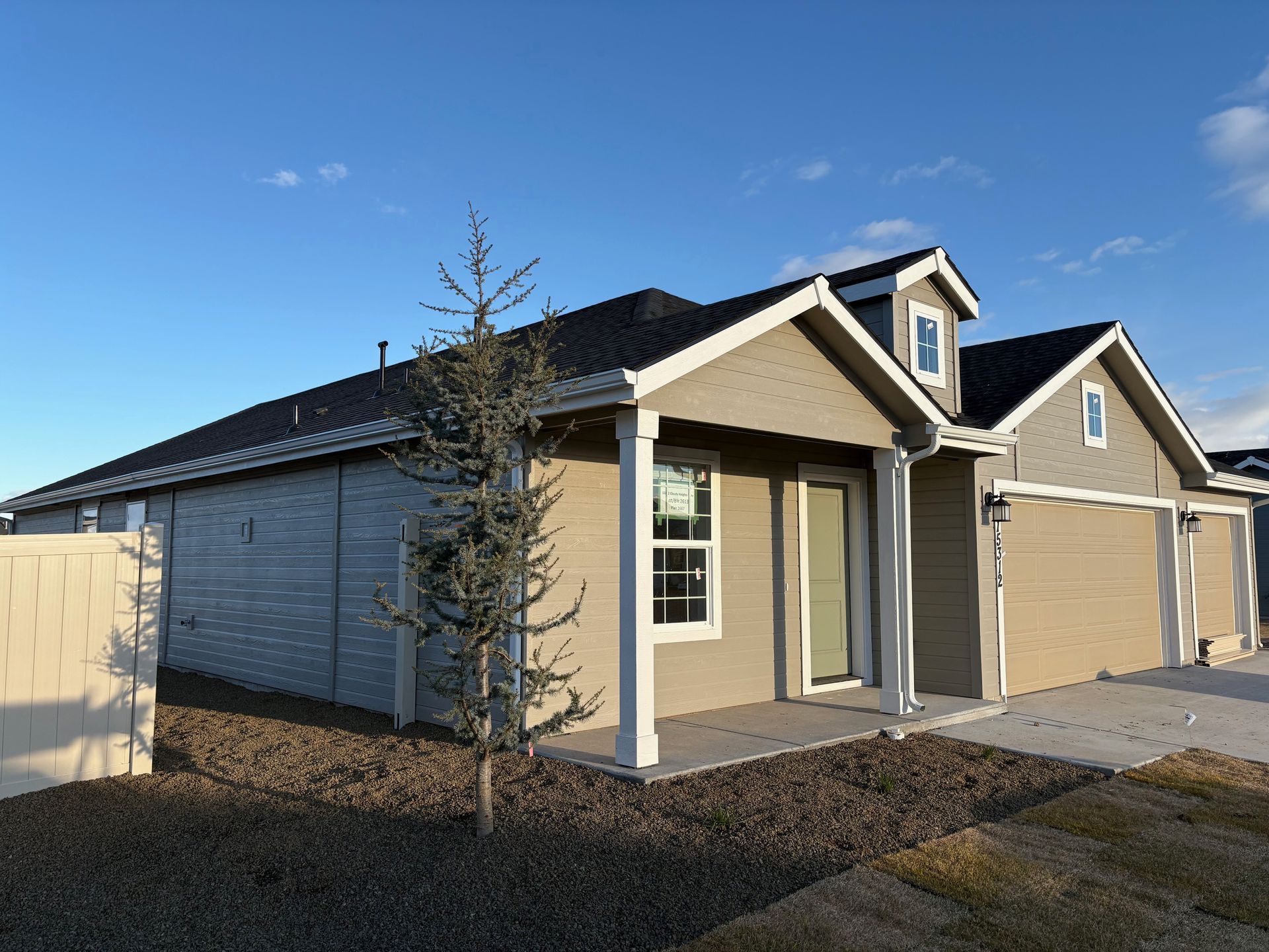 New tan and grey house with black roof, small tree, blue sky, and a garage.
