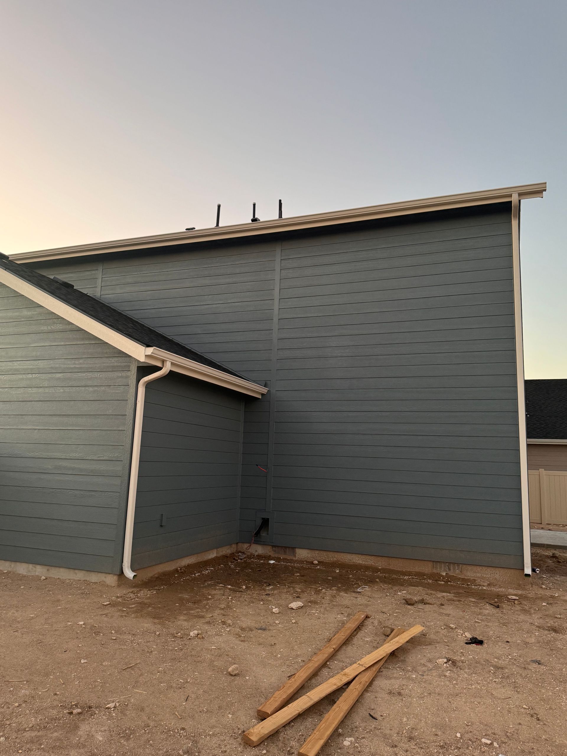Exterior of a house under construction; blue siding, white trim, with building materials on dirt ground.