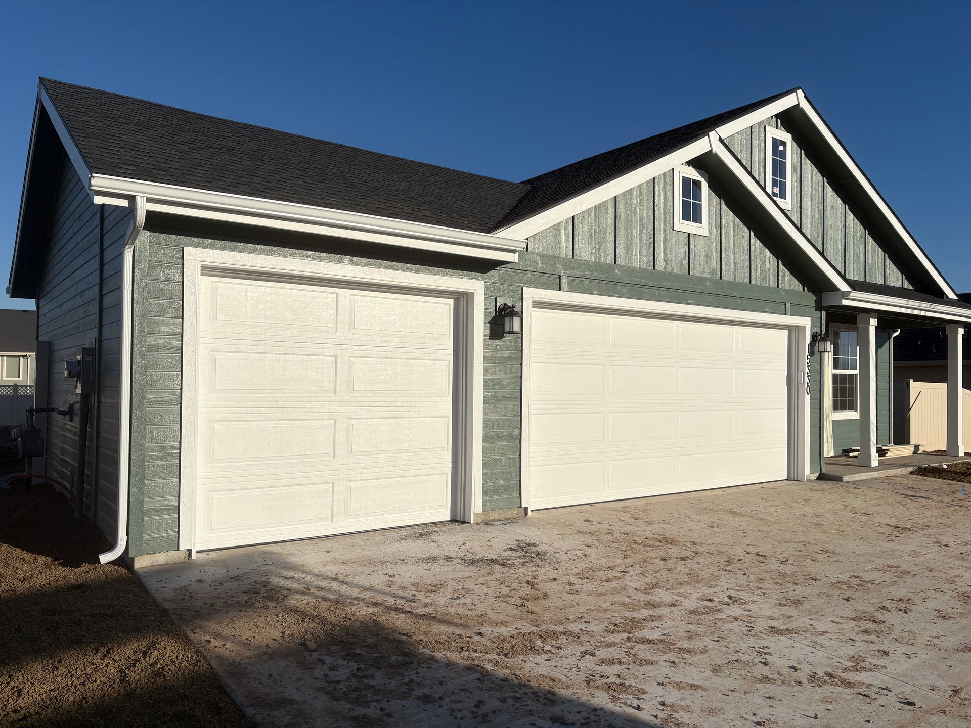 Two-car garage with white doors on a green house. Concrete driveway, blue sky.